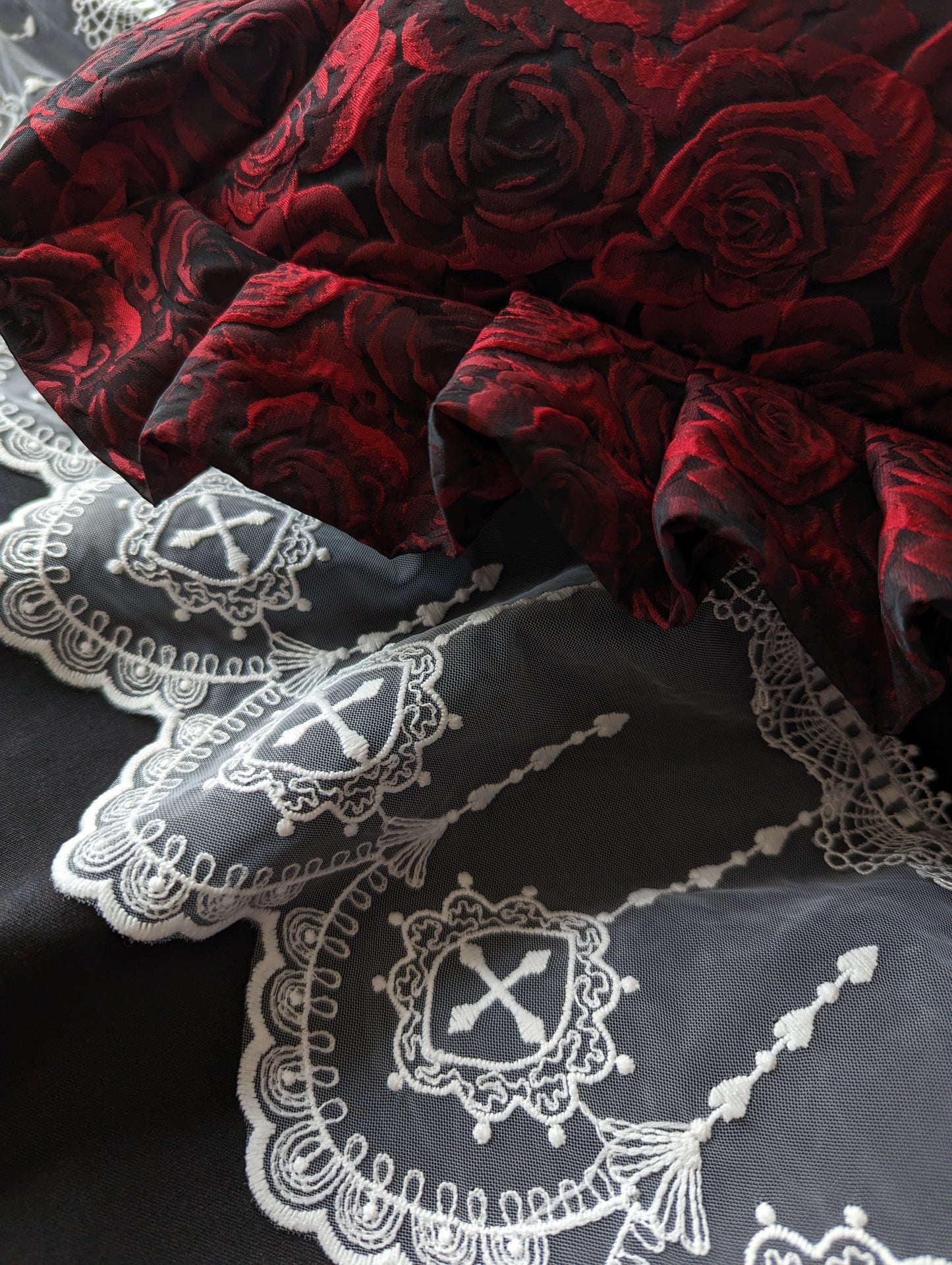 A close up of white ecclesiastical lace on black bedding, with a red rose cushion with a ruffle on top.
