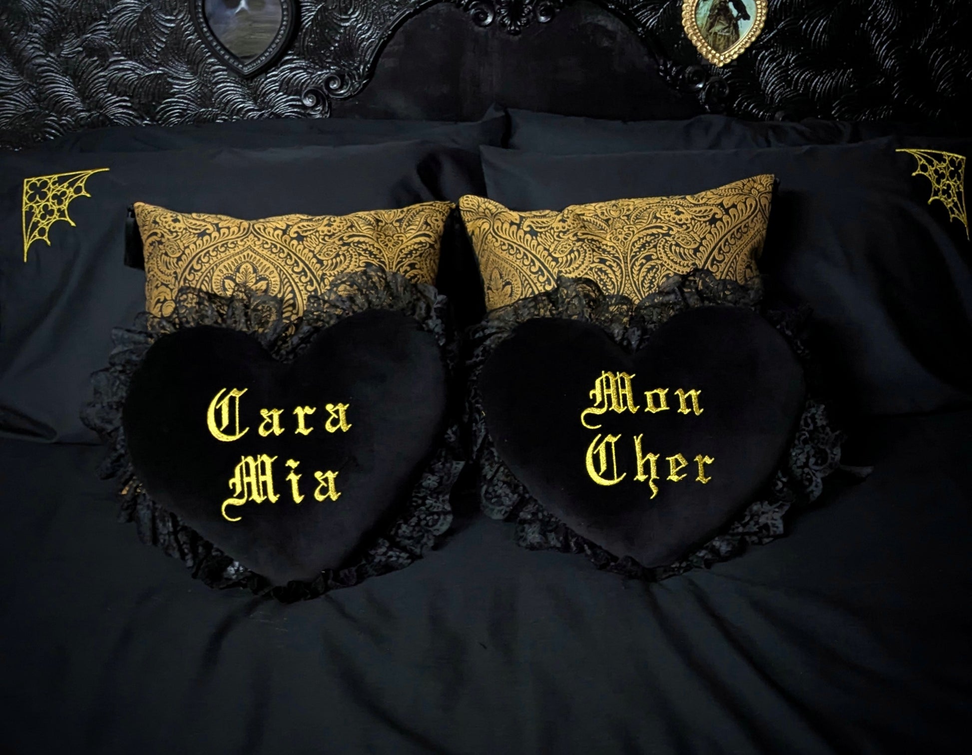 Black heart-shaped pillows with gold embroidered text on a black bed