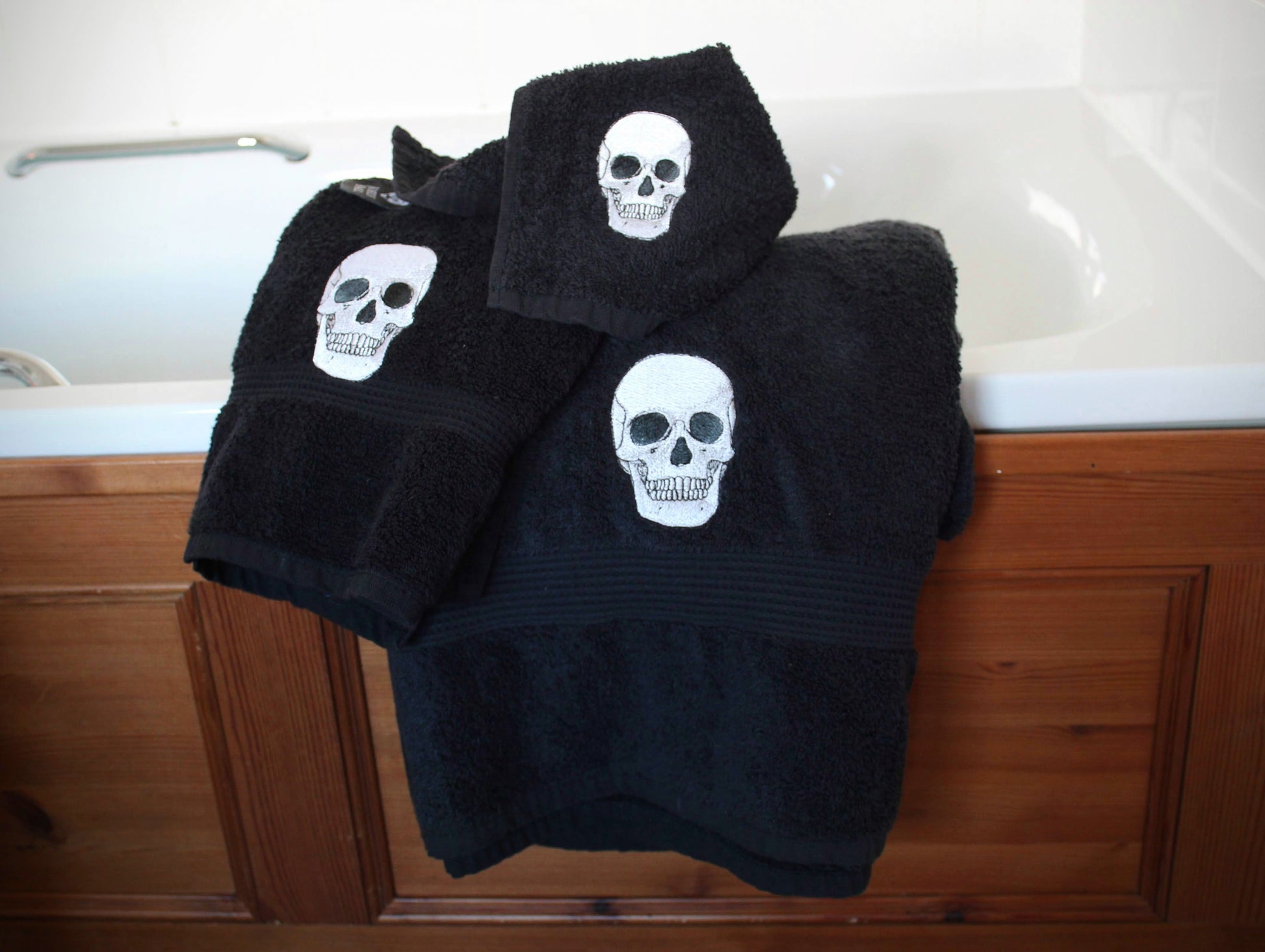 Black towel set with embroidered skulls on the side of a bath.
