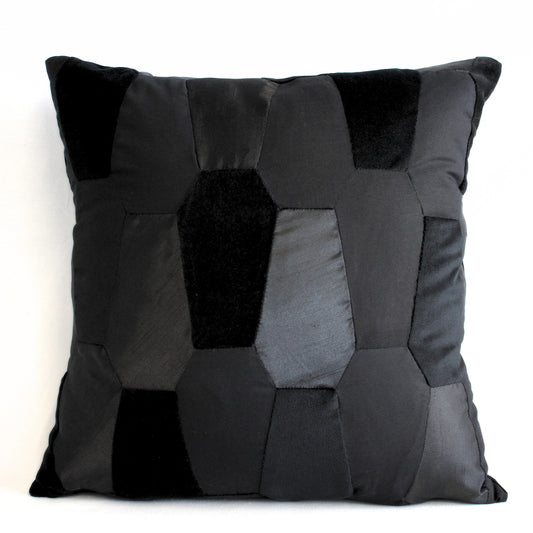 A black scatter cushion made from coffin shaped pieces of different fabric, on a white background.