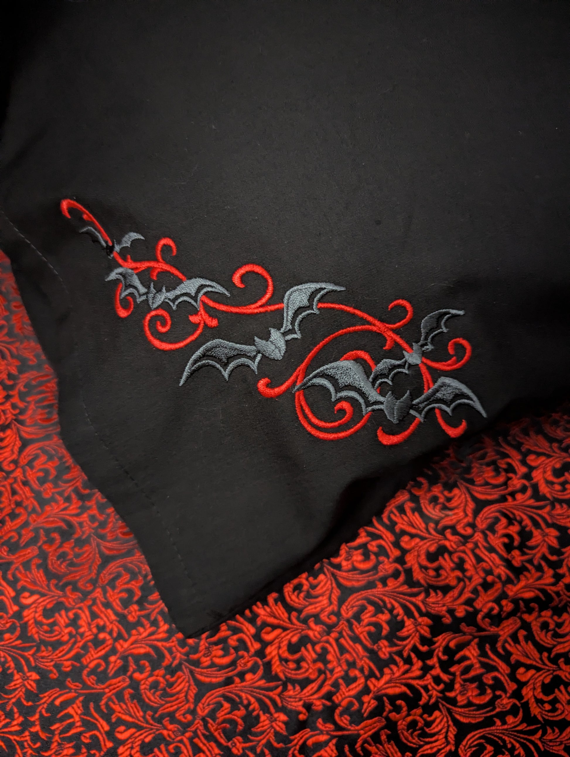 Black pillowcase with red and gray embroidered bats on a red patterned background