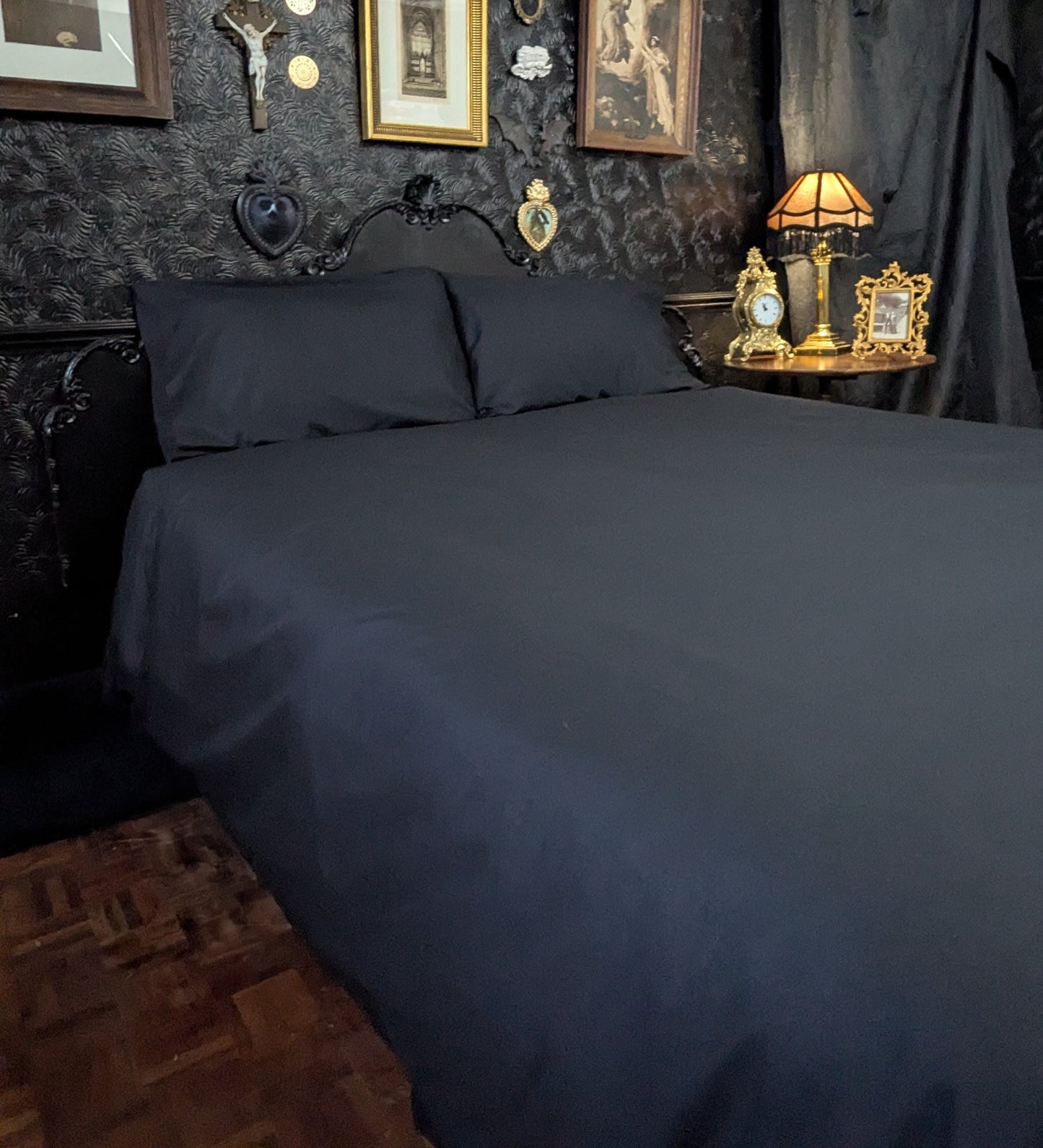 Black bedding set on a bed with decorative items on the wall and nightstand.