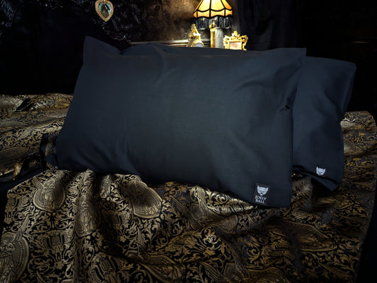 Black pillowcases on a textured fabric surface with a vintage lamp in the background.