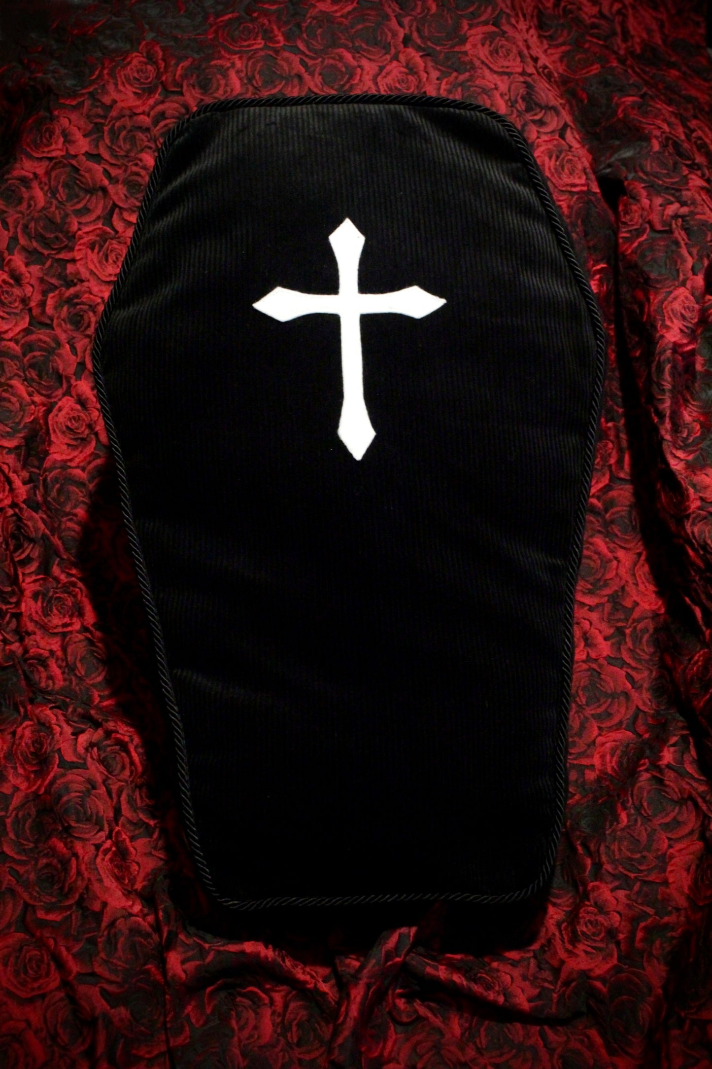 Front view of a black coffin box cushion with a white cross on a red rose background.
