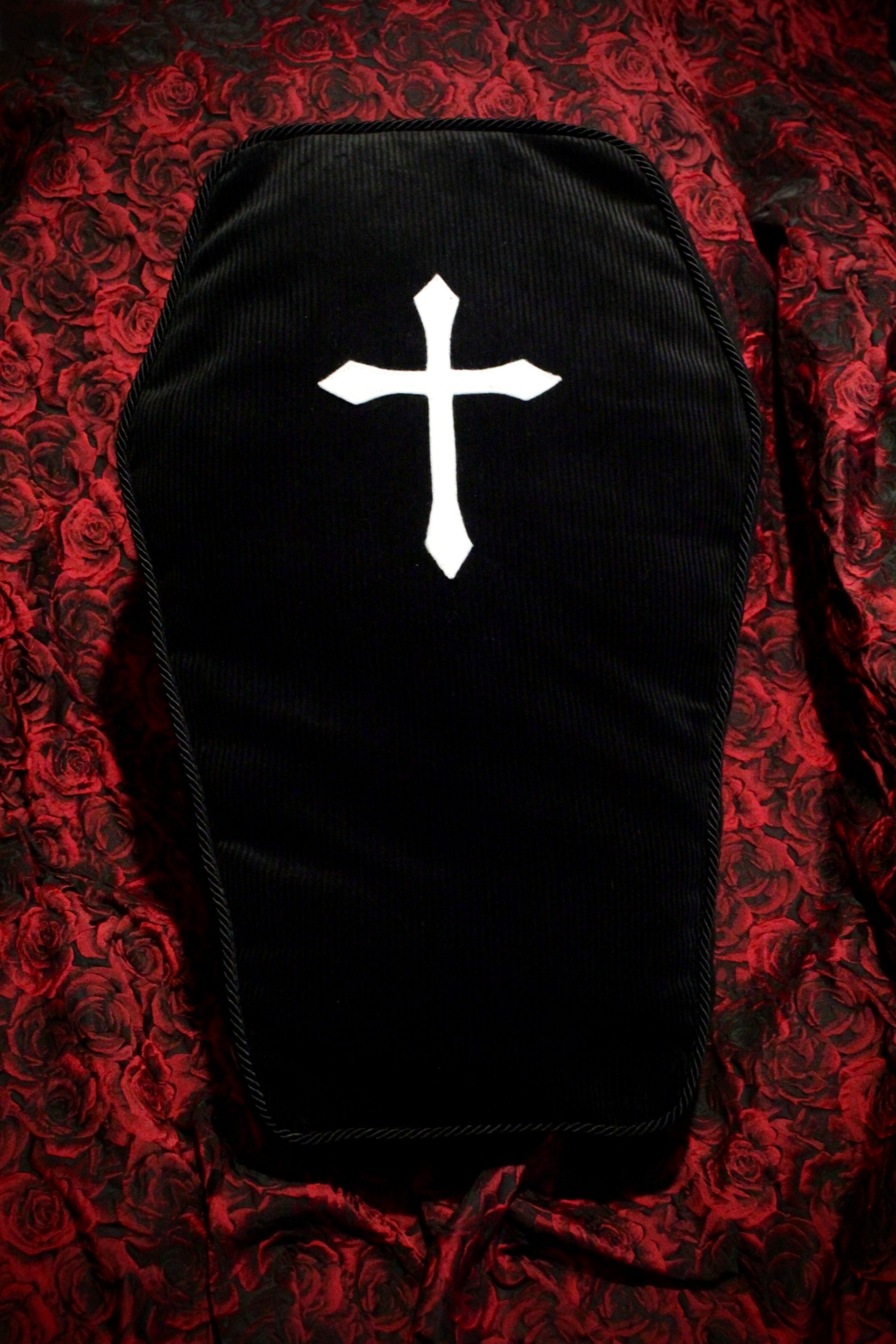 Front view of a black coffin box cushion with a white cross on a red rose background.