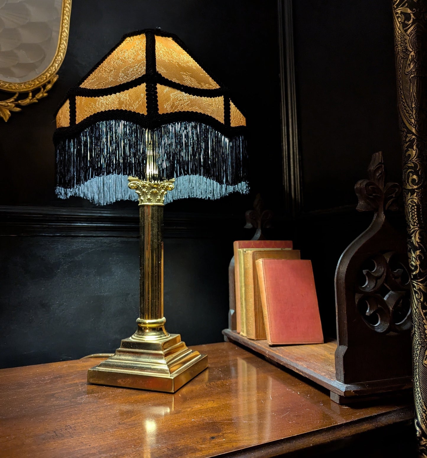 A dark academia styled corner featuring a brass lamp with a gold and black Victorian style lampshade.