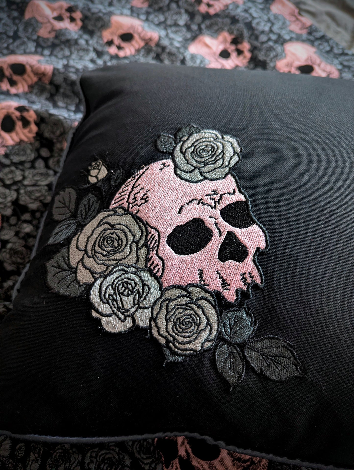 Black fabric with a pink skull and floral embroidery on a textured background.