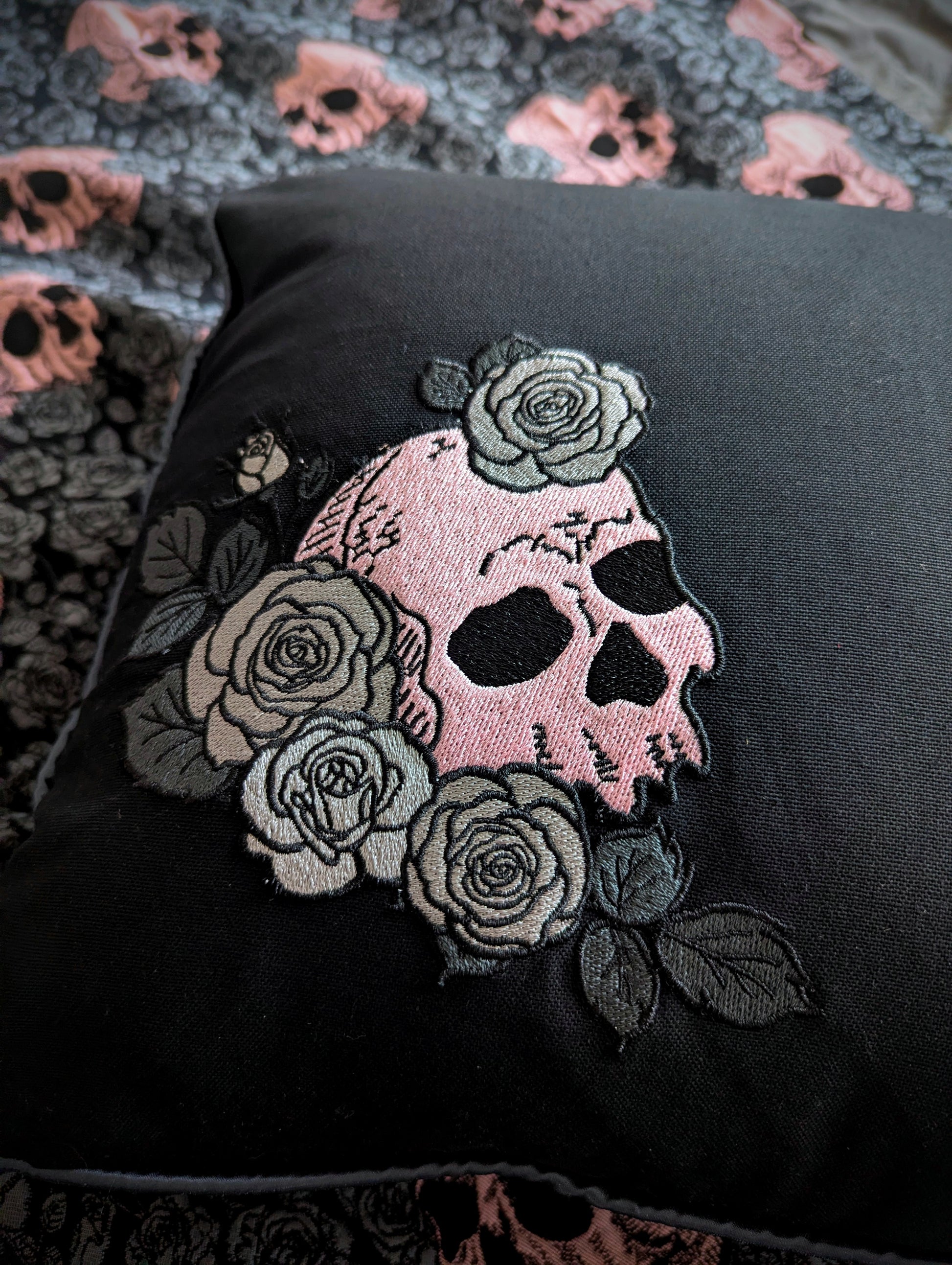 Black fabric with a pink skull and floral embroidery on a textured background.