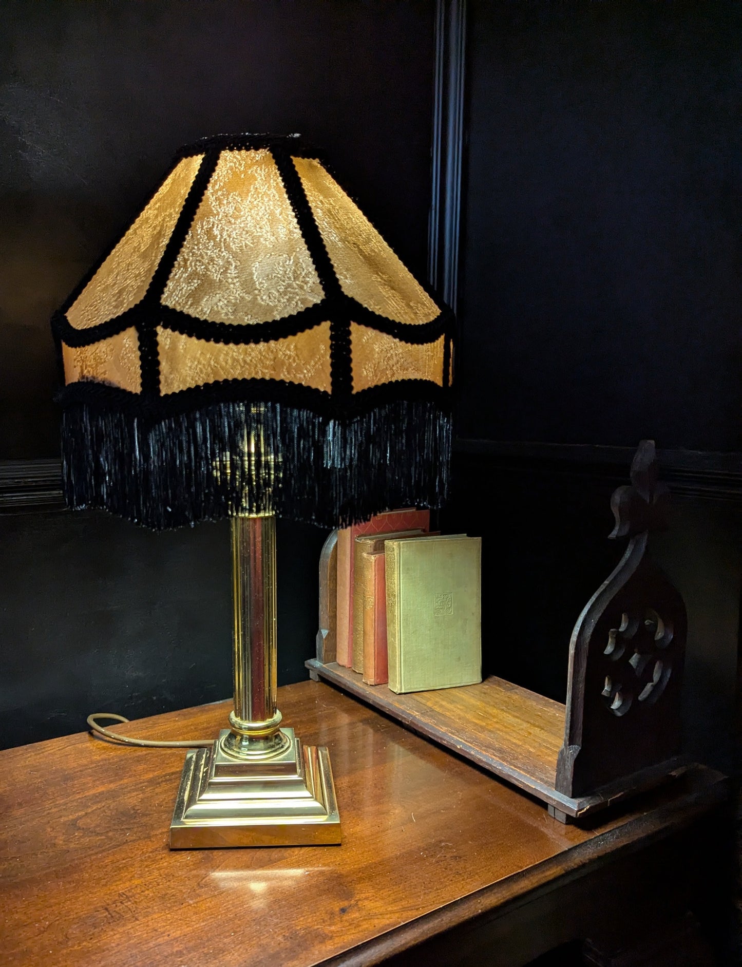 Decorative brass table lamp with a gold and black fringed shade on a wooden surface.