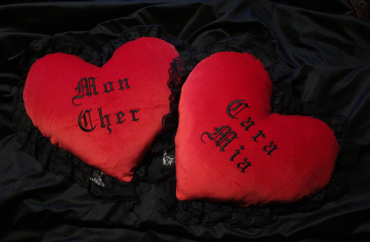 A pair of red heart shaped cushions with black lace trim, that say Mon Cher and Cara Mia.