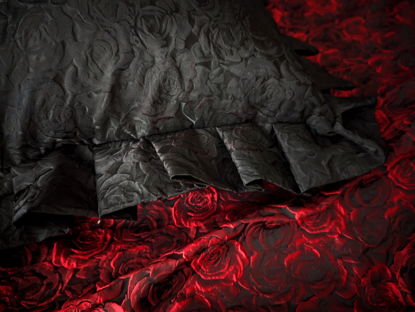 Close up details of a black rose textured cushion with ruffles with red rose fabric in the background.