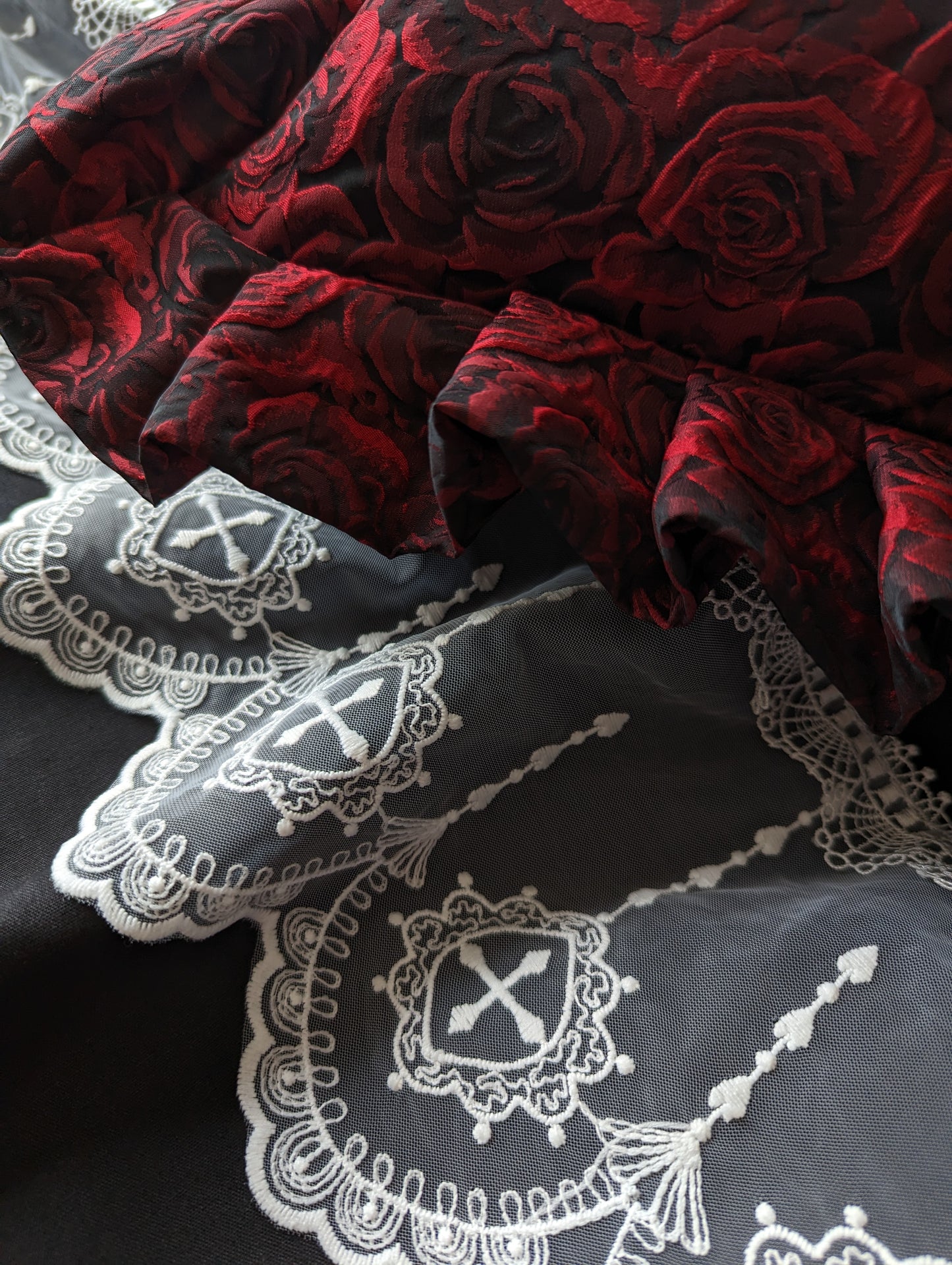 Close up details of our Mourning Parlour lace, showing it's pretty scalloped edge and cross details. A red ruffled cushion is visible above.