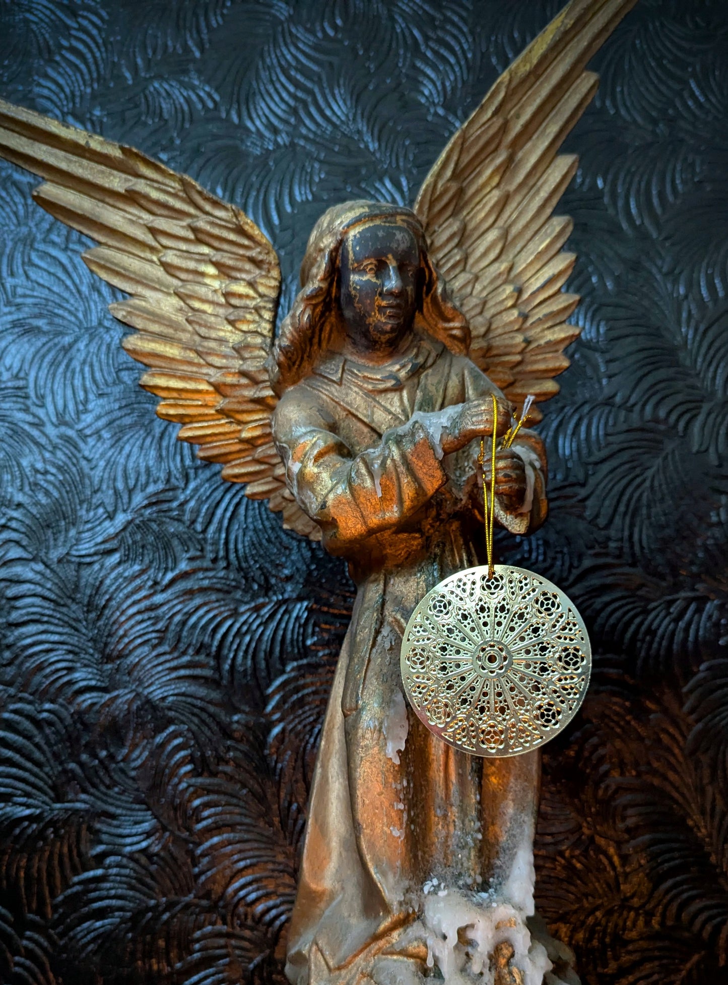 Statue of an angel holding a Gothic window ornament against a textured dark background.