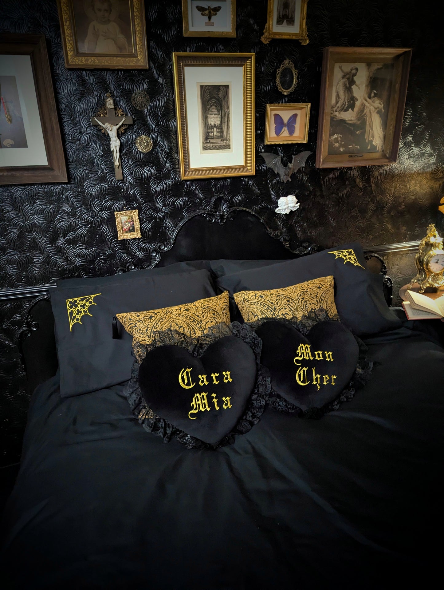 Gothic bedroom with black bedding and decorative pillows with gold text and patterns.