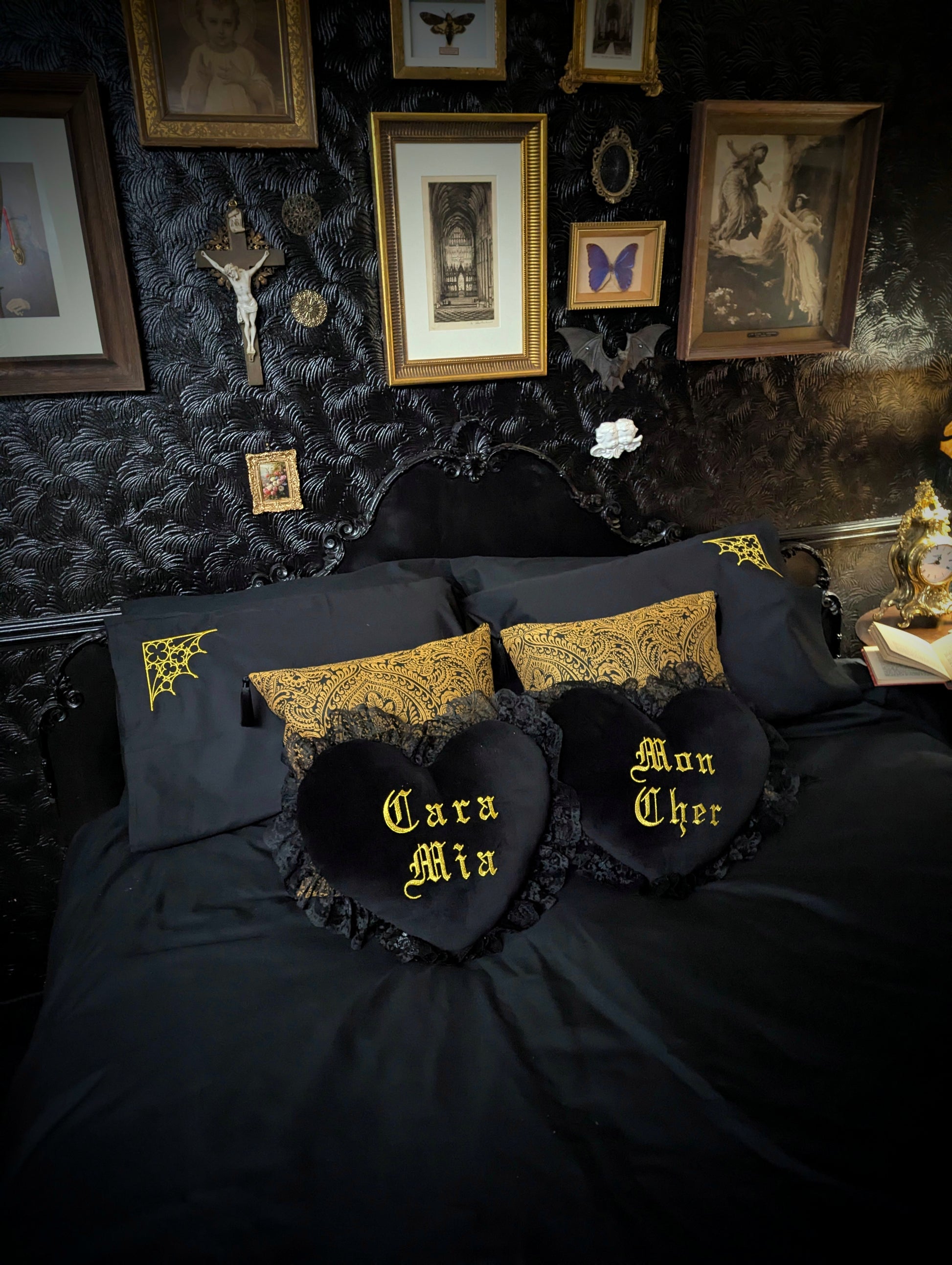 Gothic bedroom with black bedding and decorative pillows with gold text and patterns.