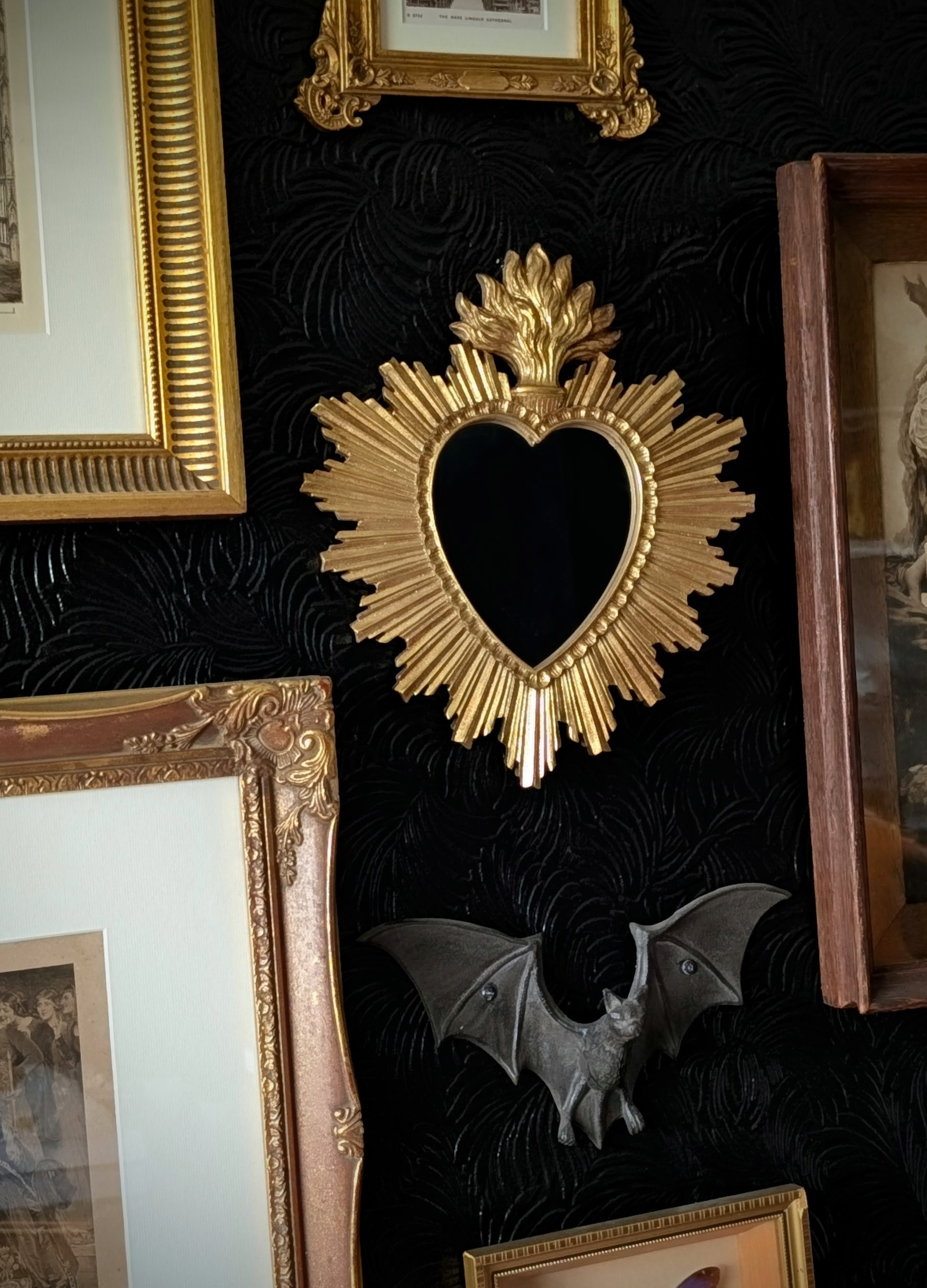 A Gothic themed gallery wall featuring a gold sacred heart mirror, bat and gold frames.