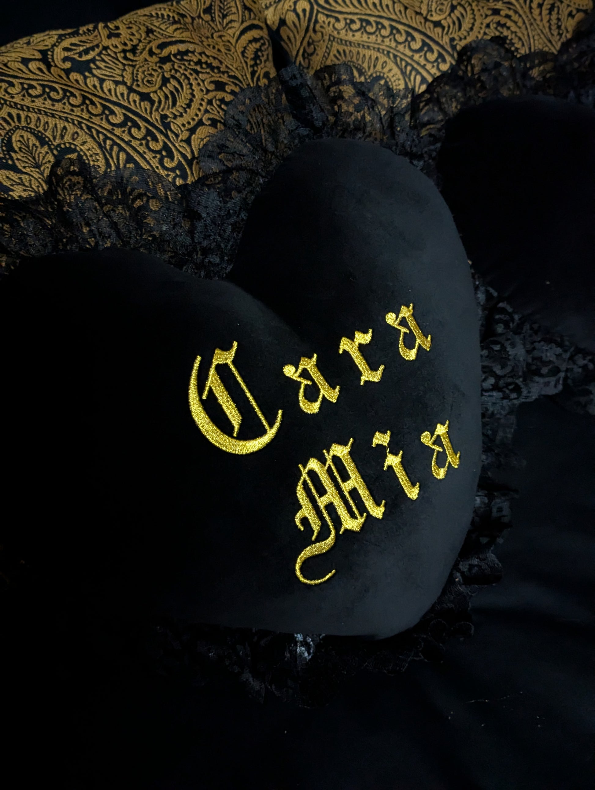 Black heart-shaped pillow with gold text on a dark background
