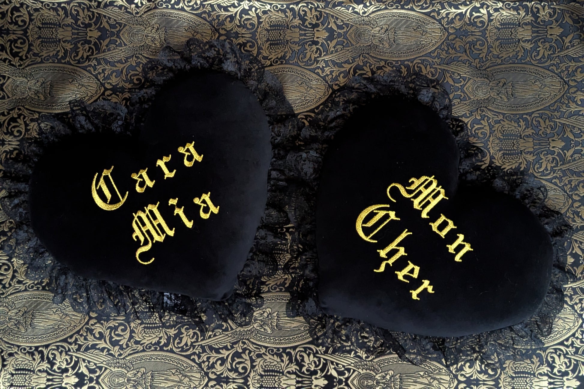 Black velvet cushions with 'Cara Mia' and 'Mon Cher' text on a patterned fabric background