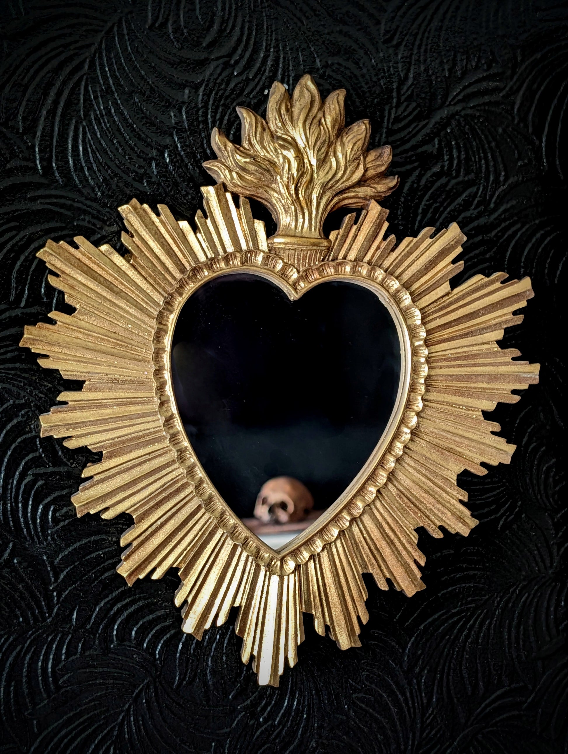 A gold mirror on a black wall with a reflection of a skull