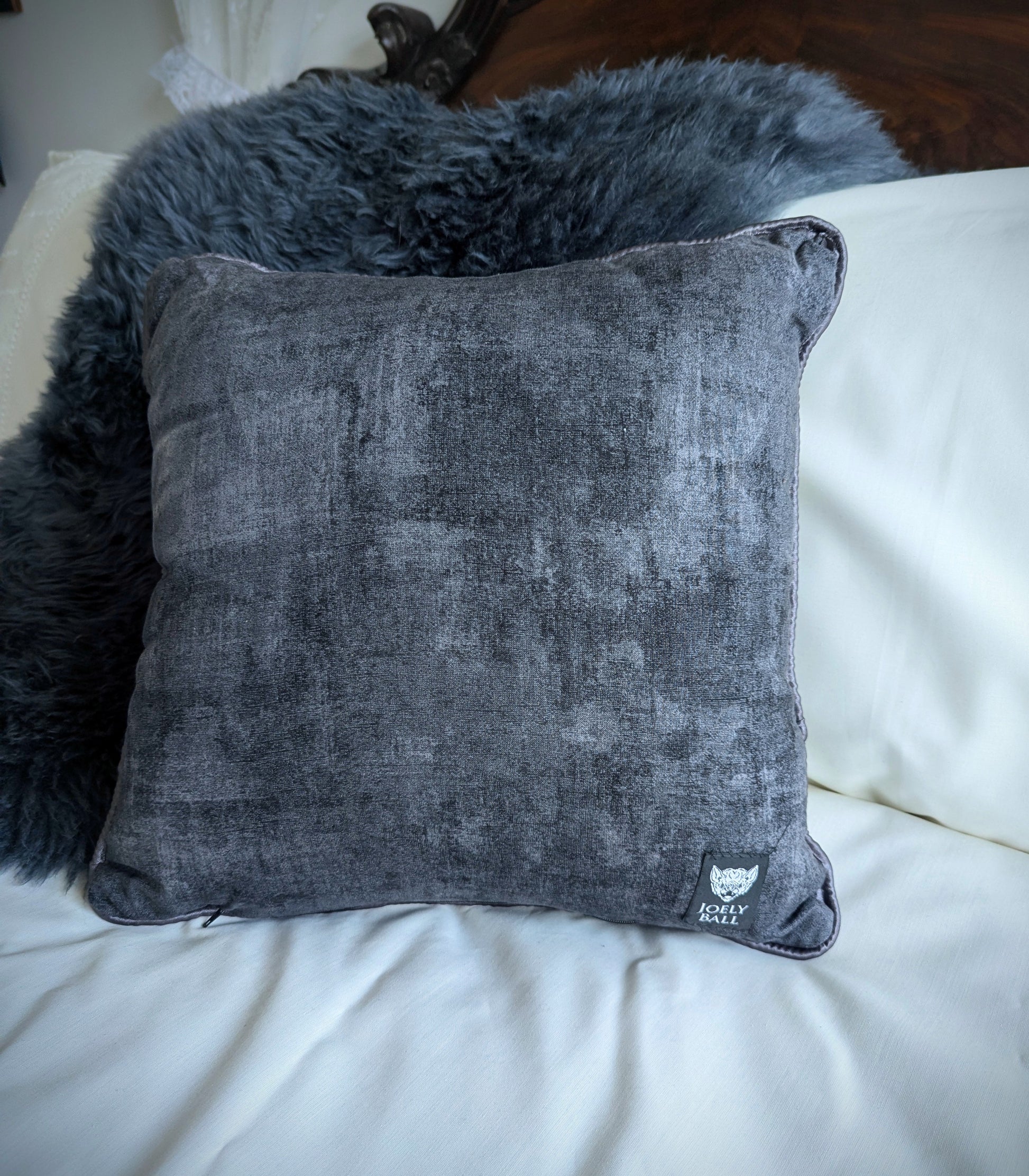 Gray textured pillow with a brand logo on a white surface