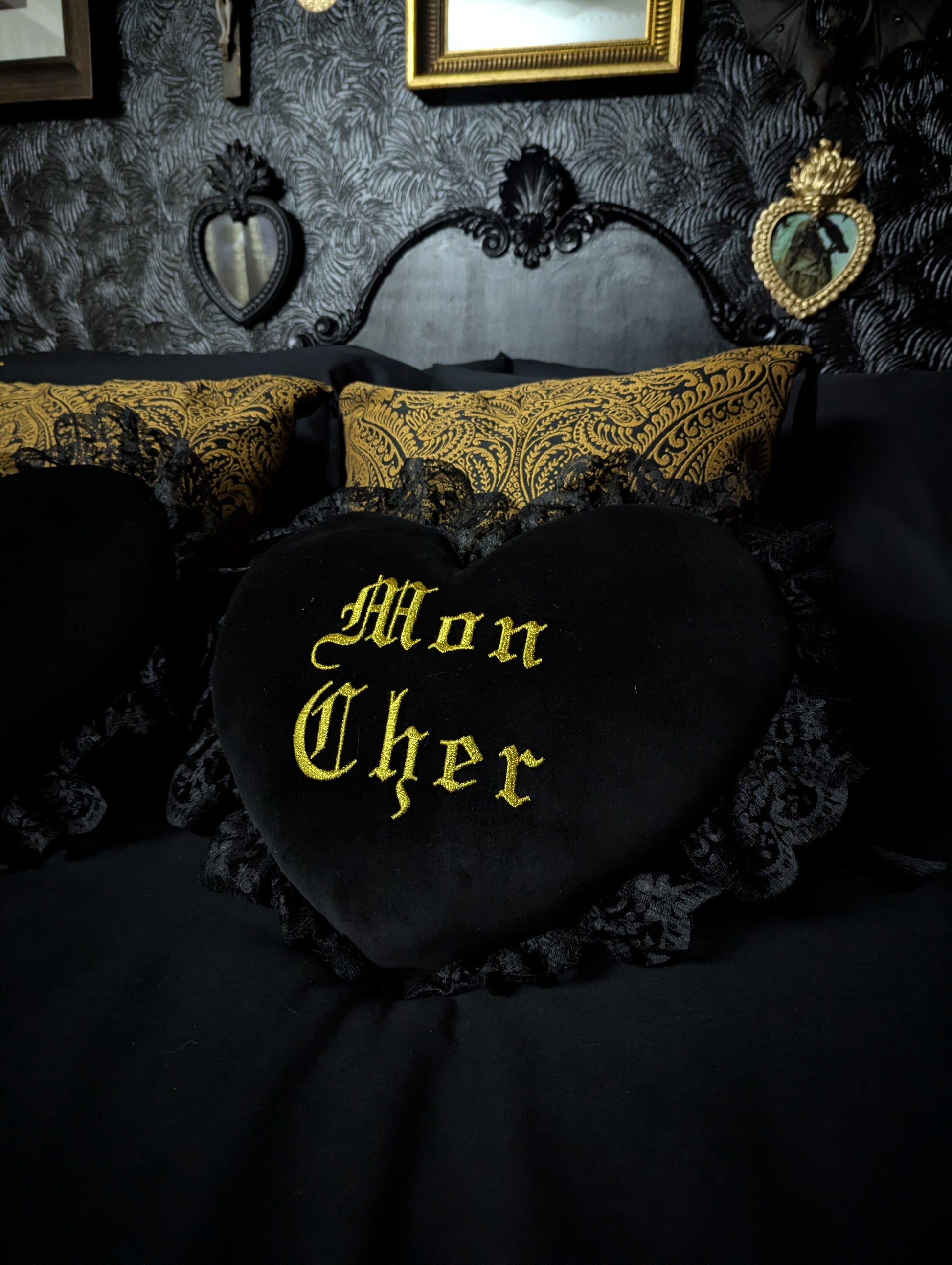 Decorative pillow with 'Mon Cher' text embroidered in gold on a dark, ornate headboard.