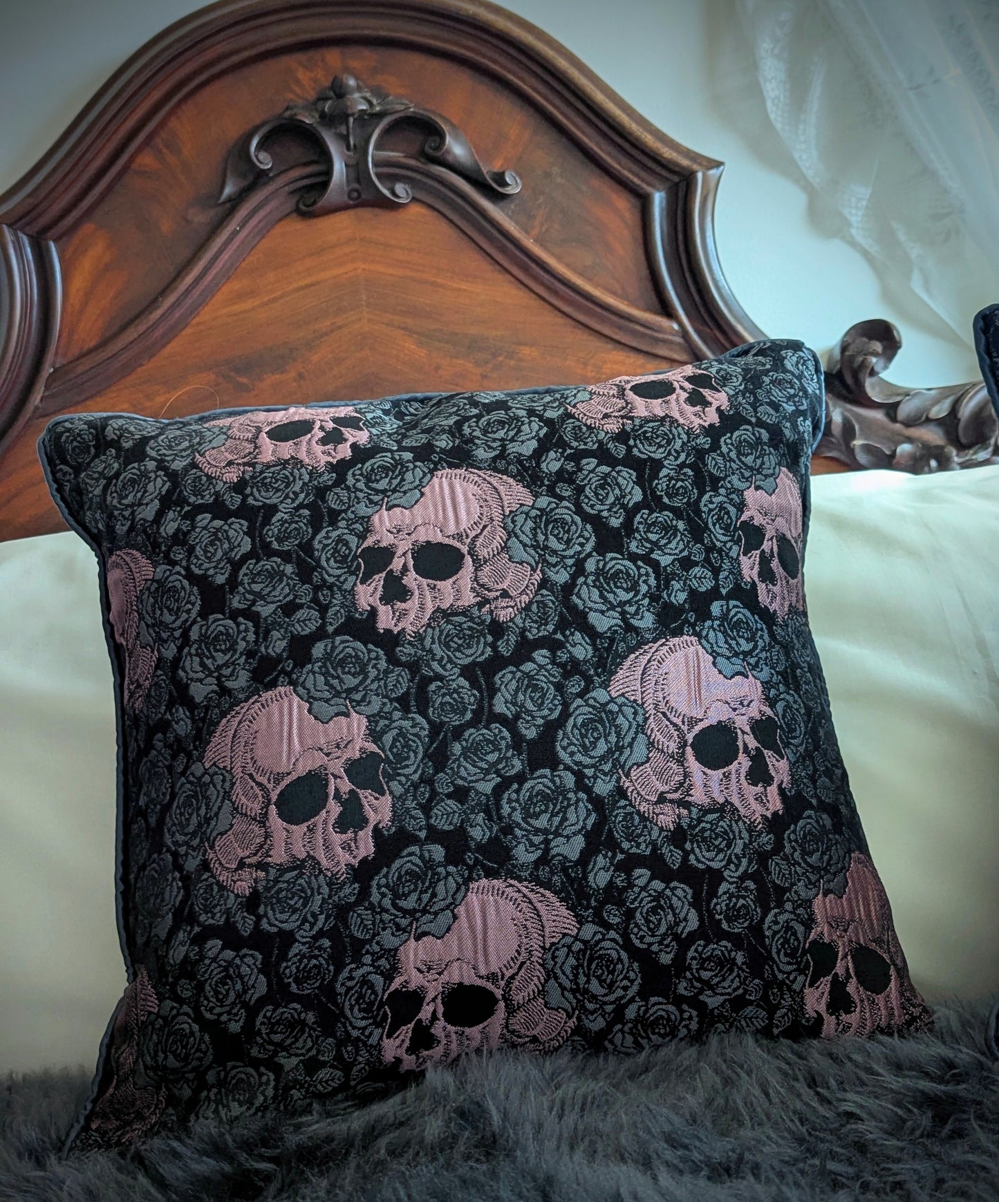 Decorative pillow with skull and rose pattern on a bed with wooden headboard