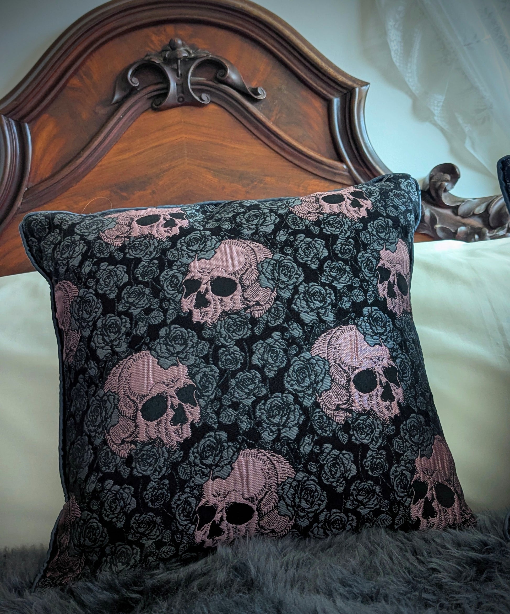 Decorative pillow with skull and rose pattern on a bed with wooden headboard