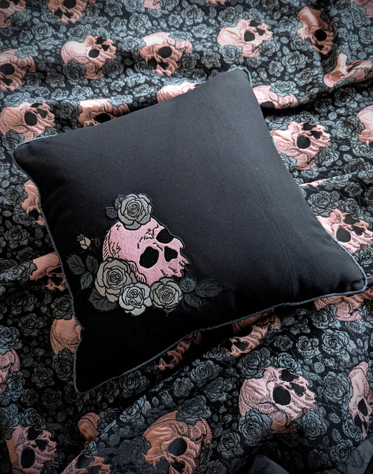 Black pillow with skull and floral design on a patterned fabric background