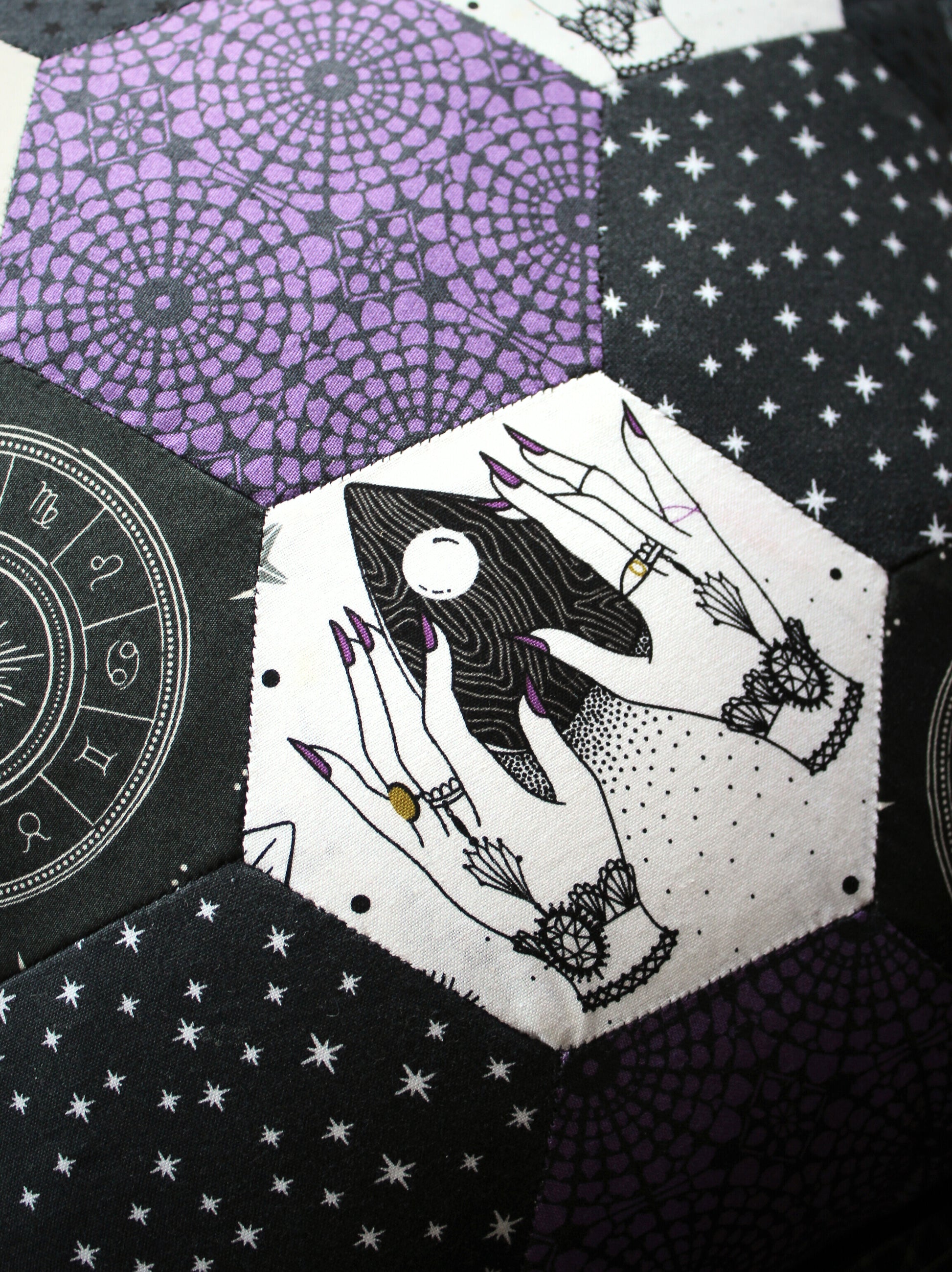 Close up of a hexagon patchwork, featuring a planchette design, stars and what looks like purple Gothic windows.