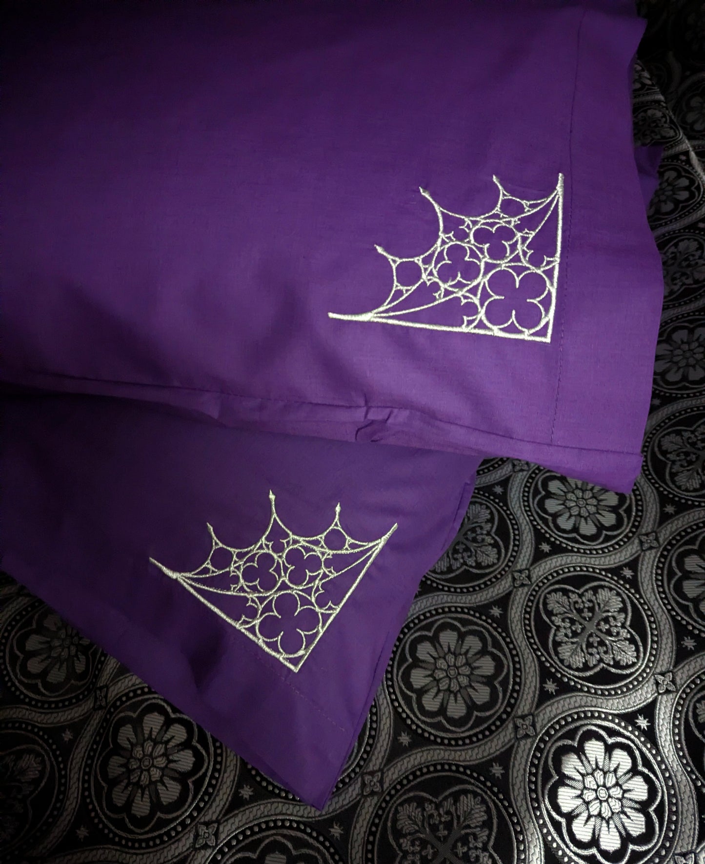 Two purple pillows with silver Gothic architecture designs on a patterned fabric background