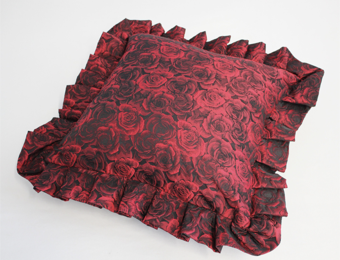 A red and black floral cushion with a ruffle around the edge.