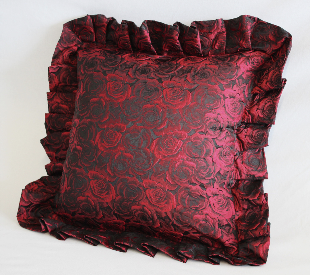 A red rose jacquard cushion with a ruffle around the edge.
