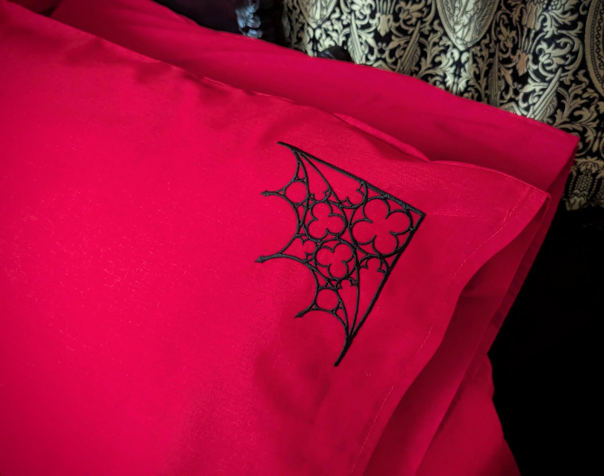 Red pillowcase with an embroidered Gothic tracery in the top corner.