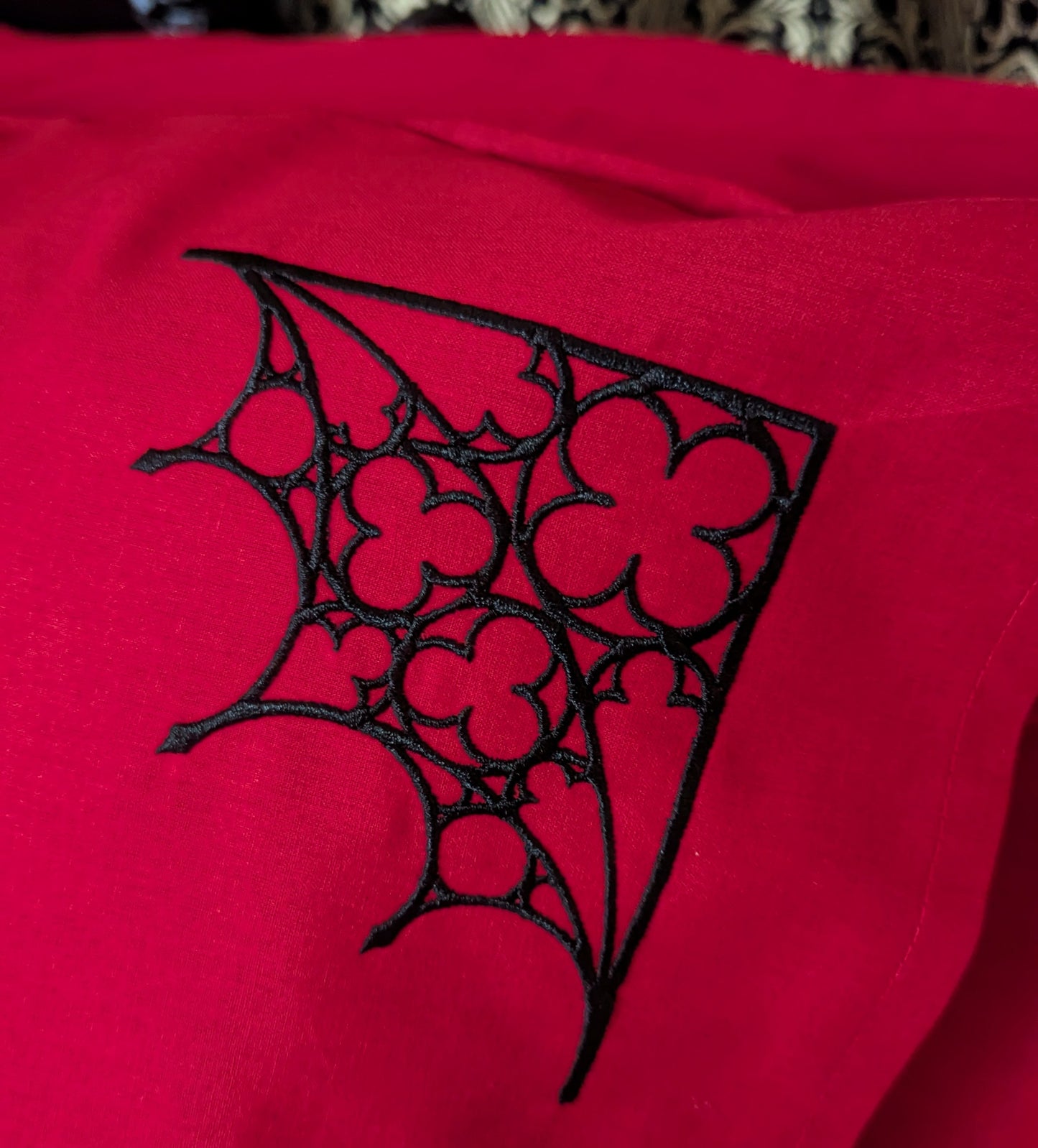 Detail shot of a red pillowcase embroidered with a black Gothic tracery design in the corner.