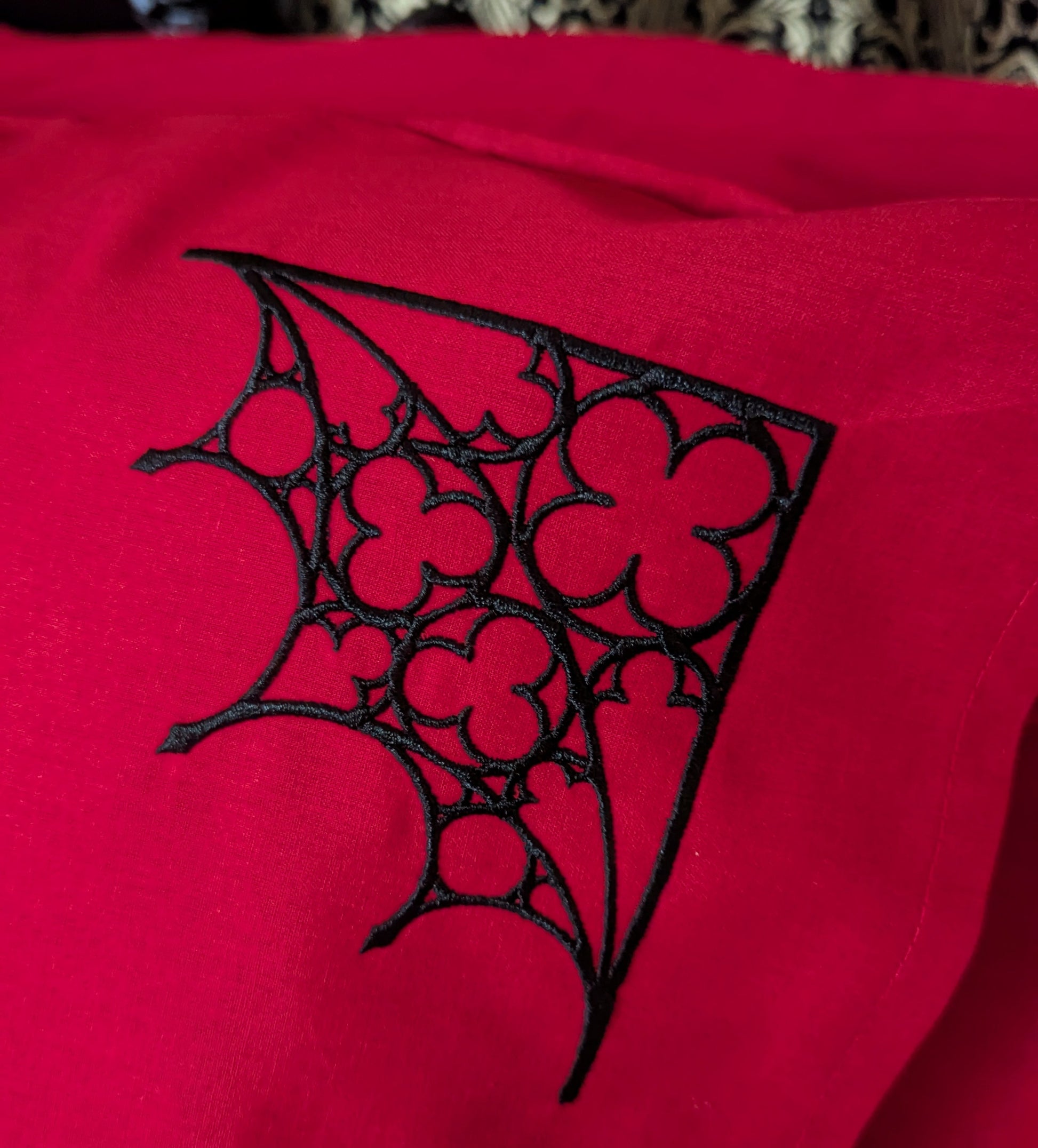 Detail shot of a red pillowcase embroidered with a black Gothic tracery design in the corner.