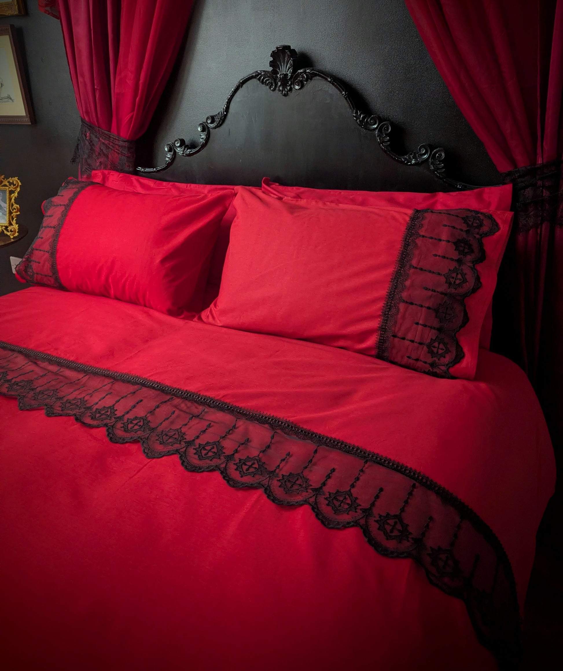Red bedspread with black lace trim on a bed against a dark wall with red curtains.