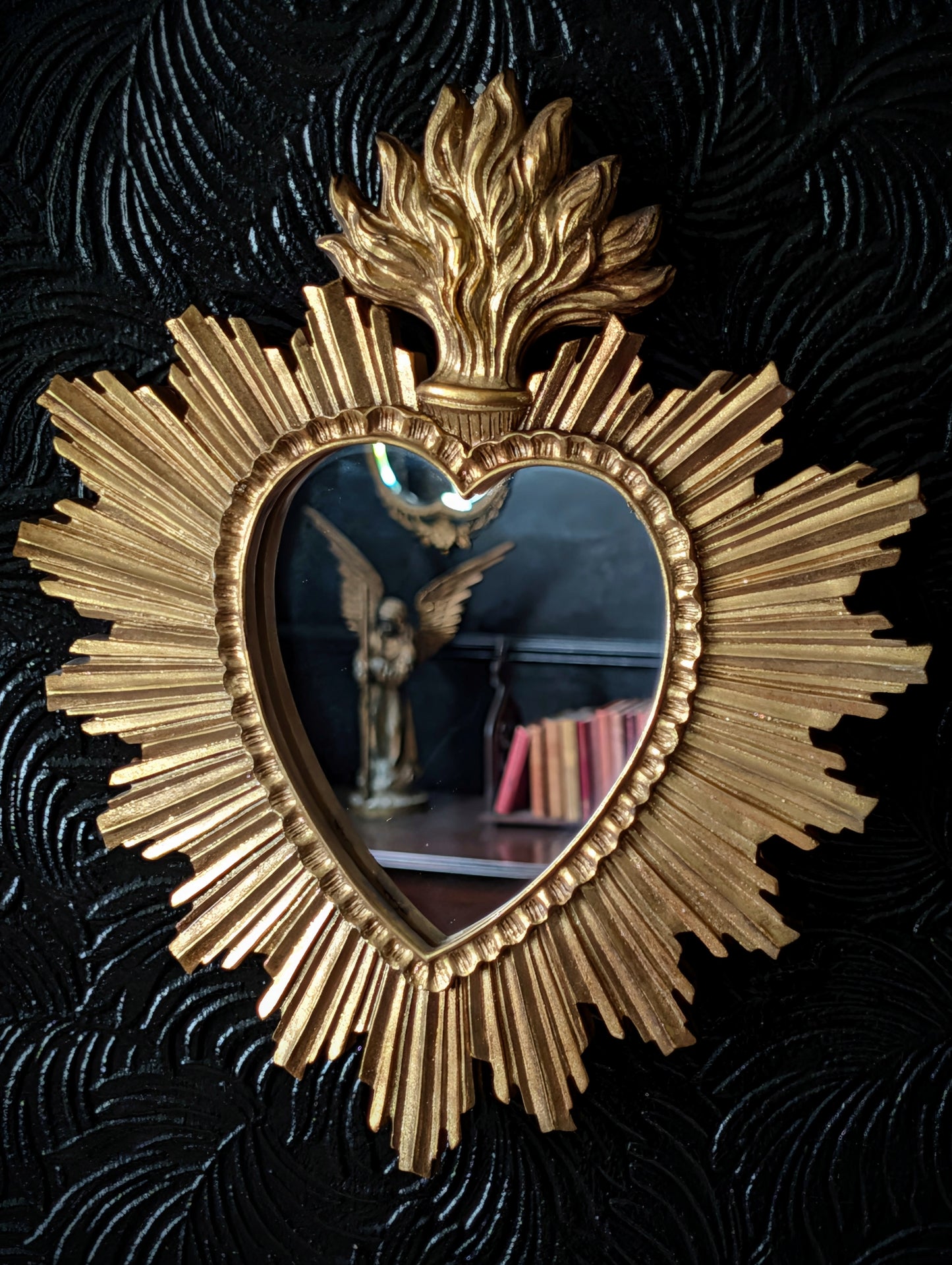 A gold sacred heart style mirror on a black wall