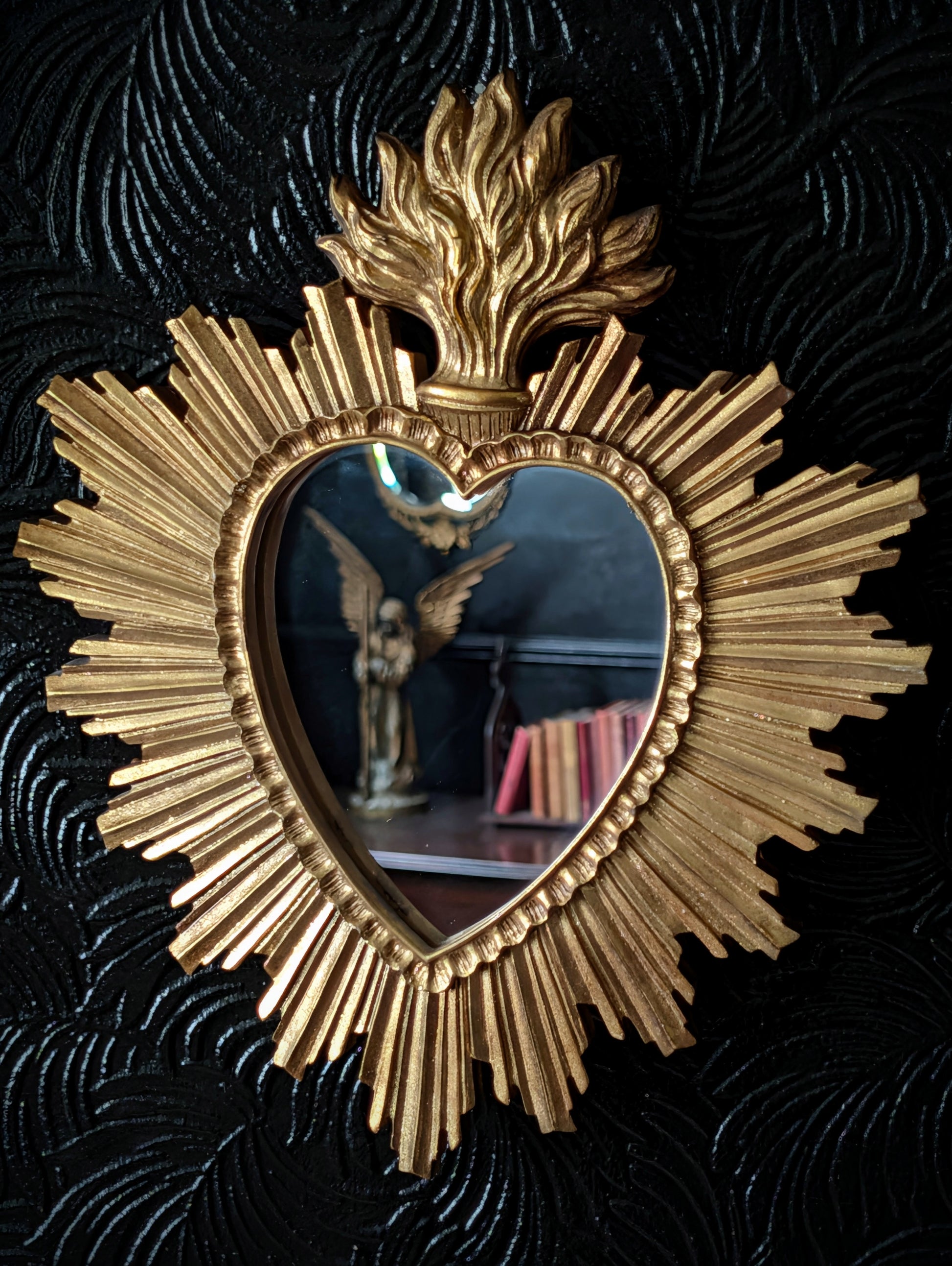 A gold sacred heart style mirror on a black wall