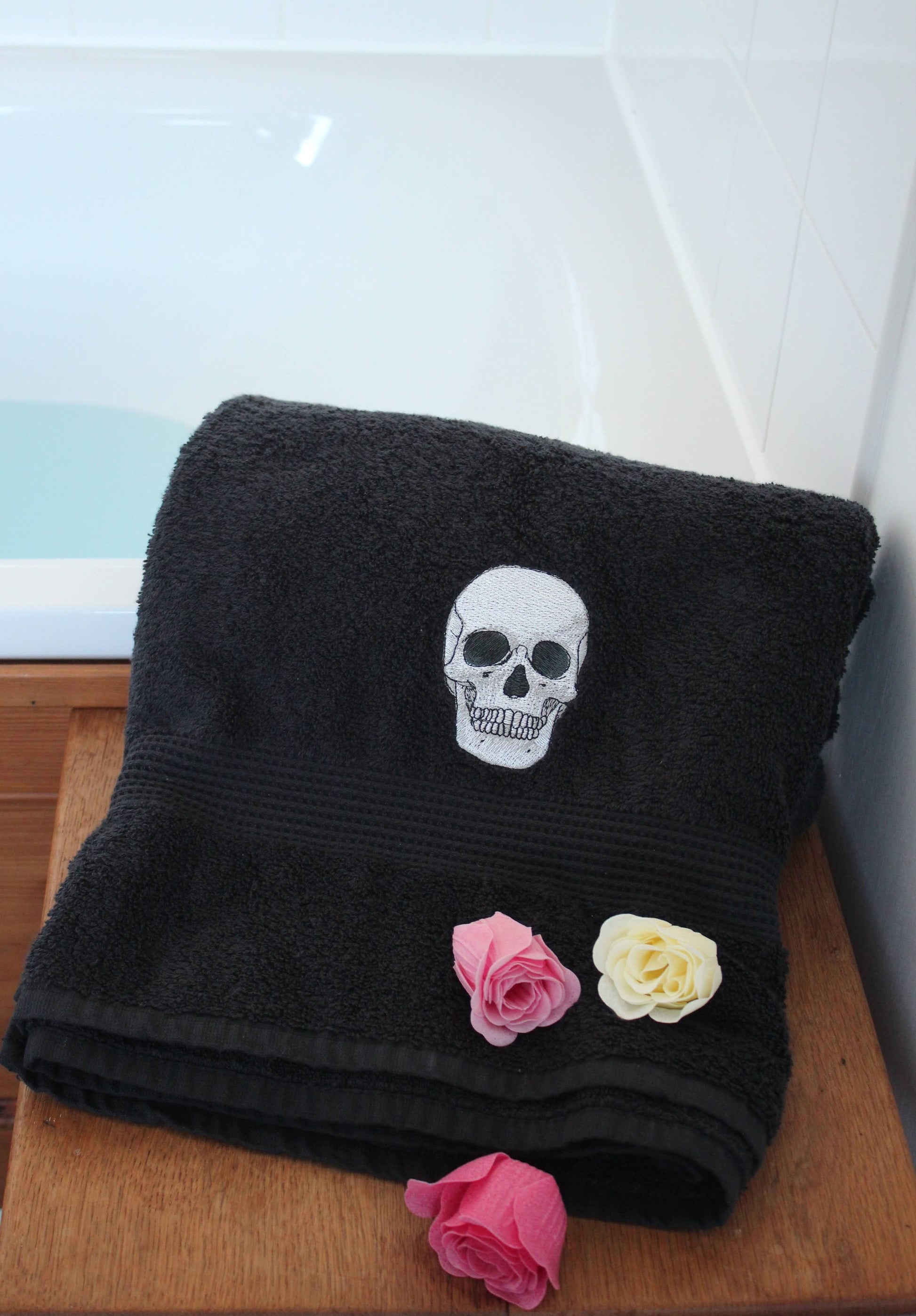 A black towel with an embroidered anatomical skull, with rose bath melts.