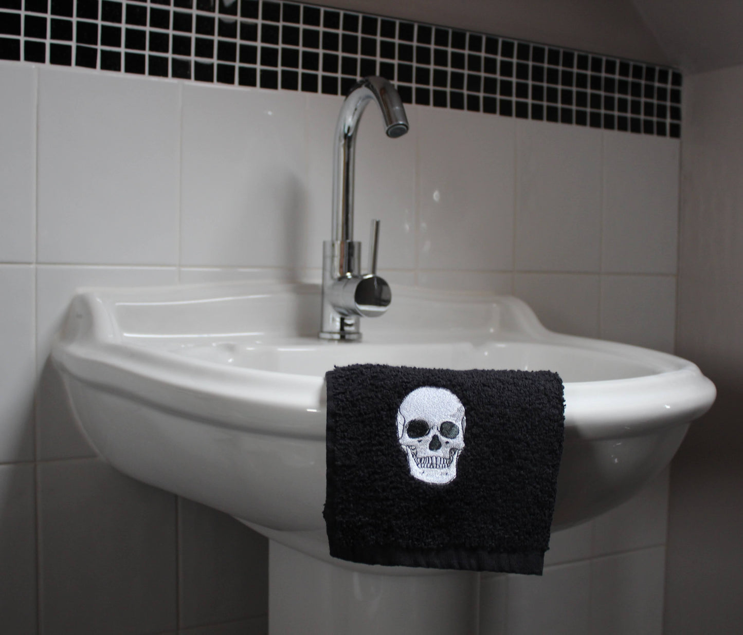 A black face cloth with an embroidered anatomical skull hanging on the edge of a bathroom sink.