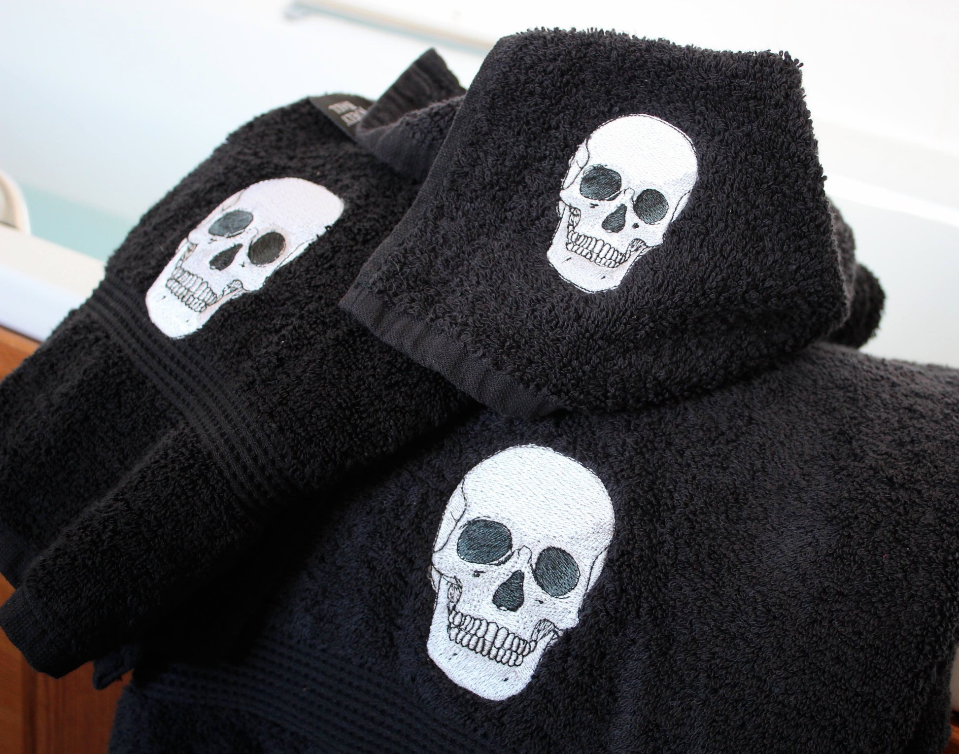 Black cotton towels with embroidered white skull designs, stacked and displayed on a surface.