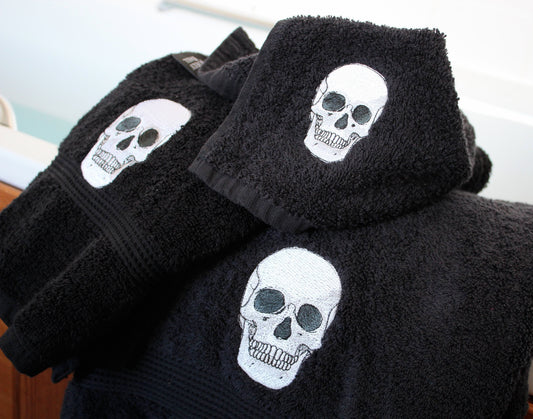Black cotton towels with embroidered white skull designs, stacked and displayed on a surface.