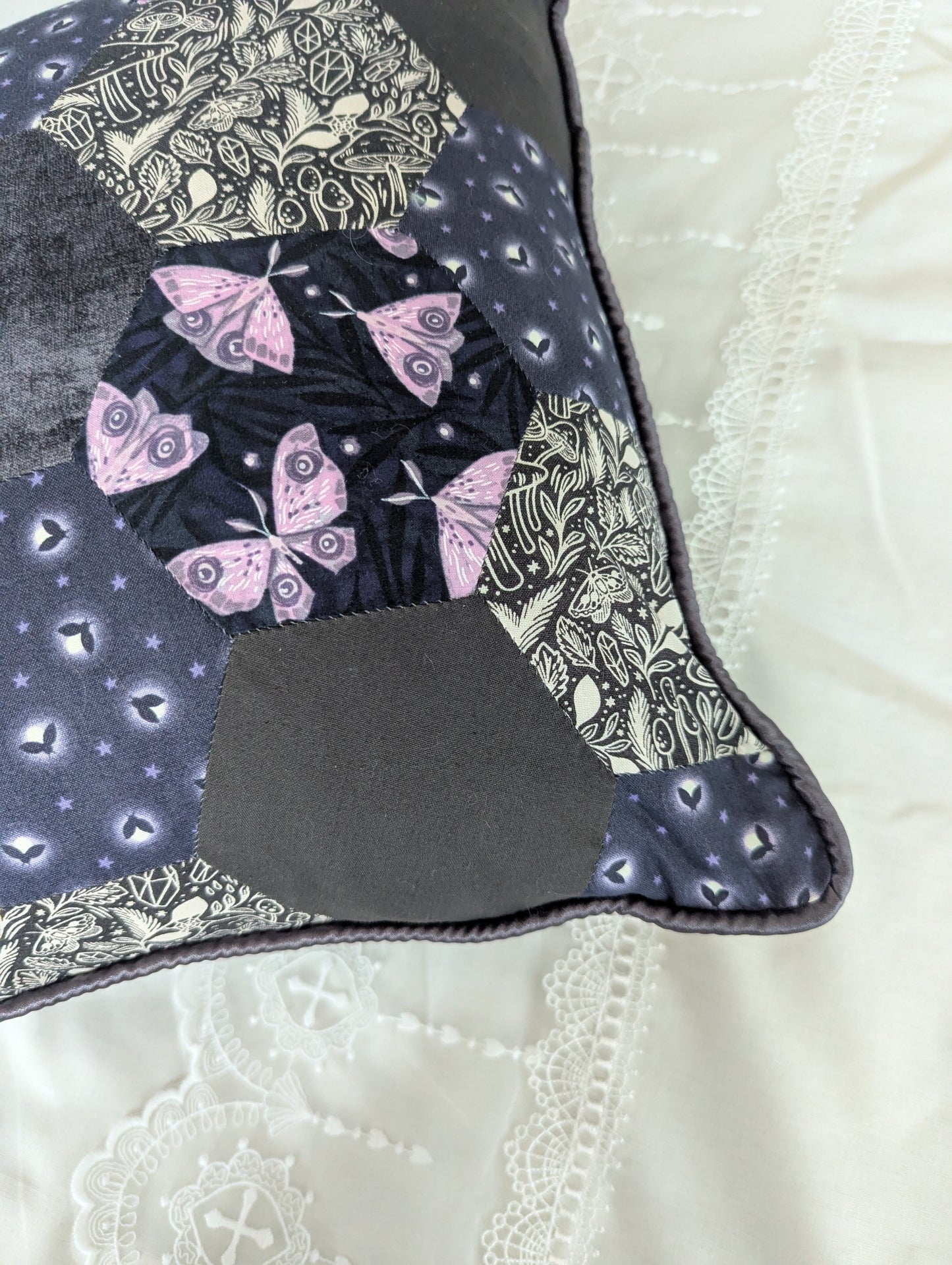 Patchwork pillow with moth design on a white lace bed set