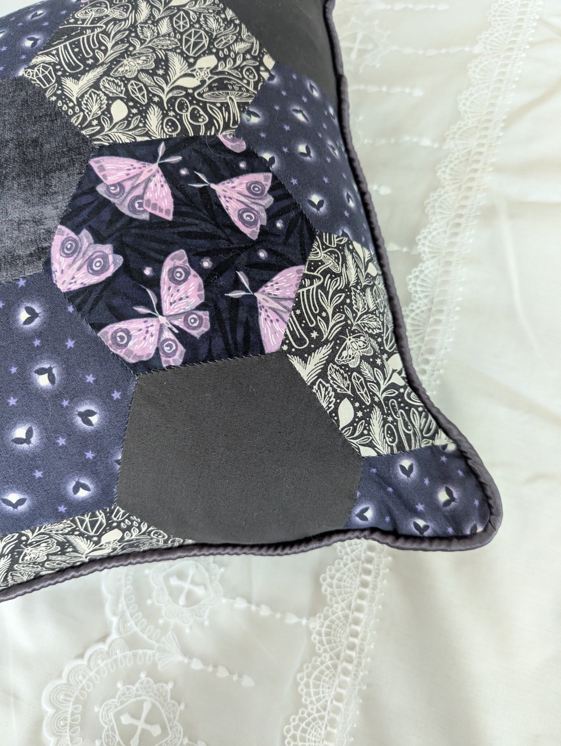 Patchwork pillow with moth design on a white lace bed set