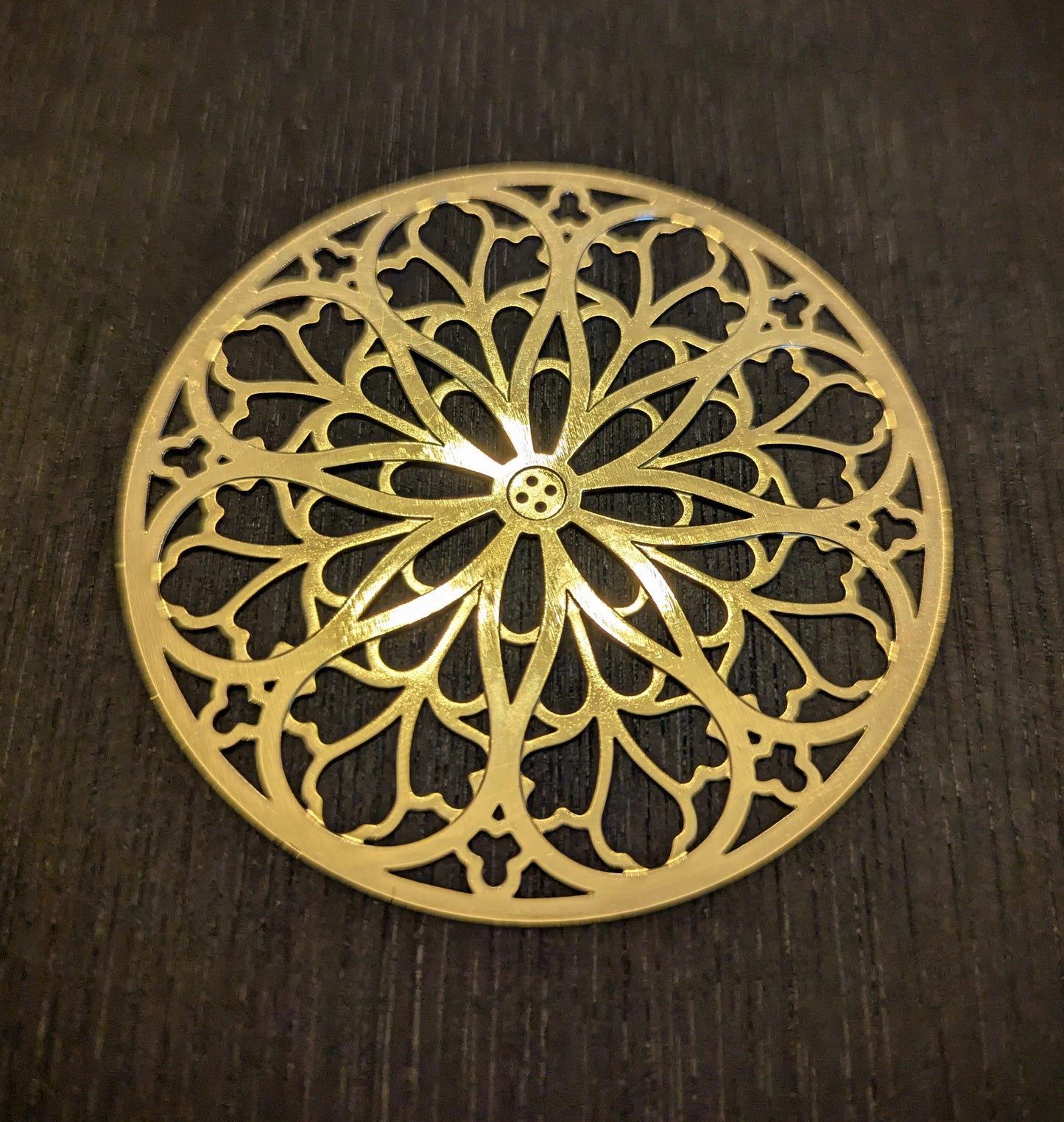 Gold decorative metal rose window with intricate patterns on a dark wooden surface