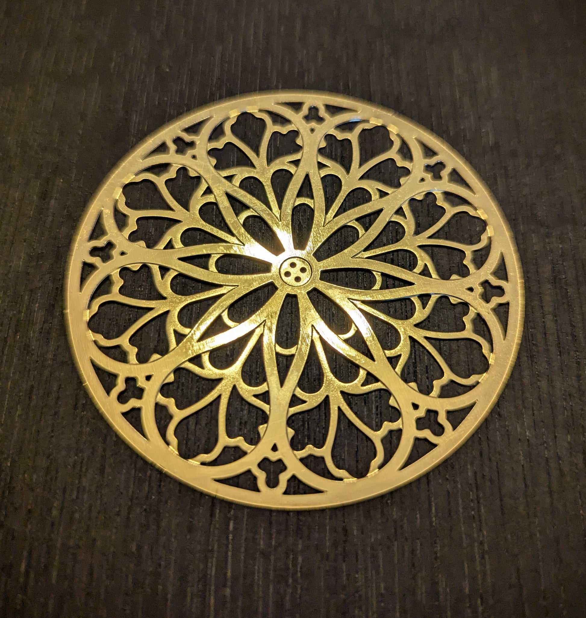 Gold decorative metal rose window with intricate patterns on a dark wooden surface
