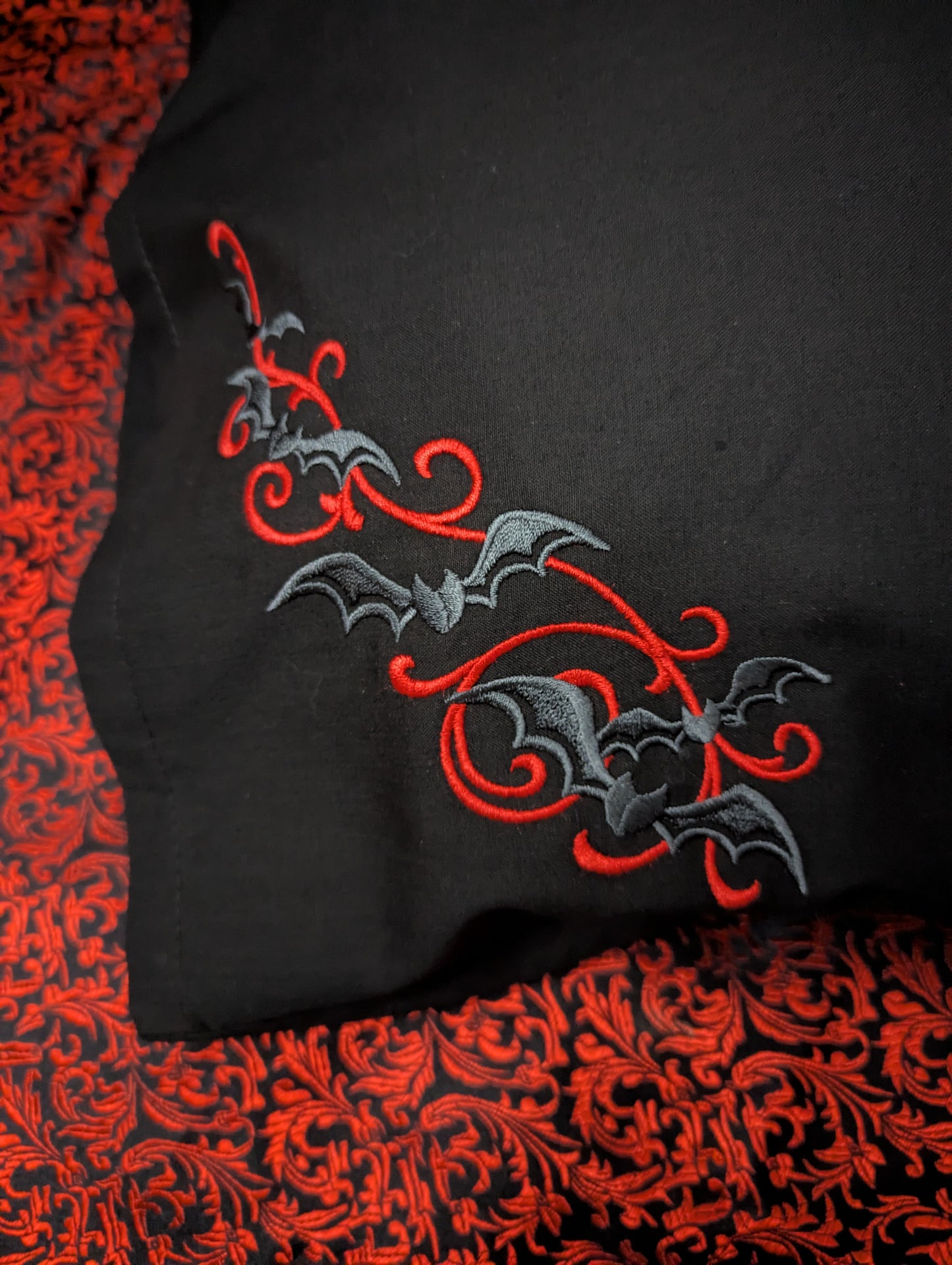 Grey bats and red scrolls embroidered on a black pillowcase 