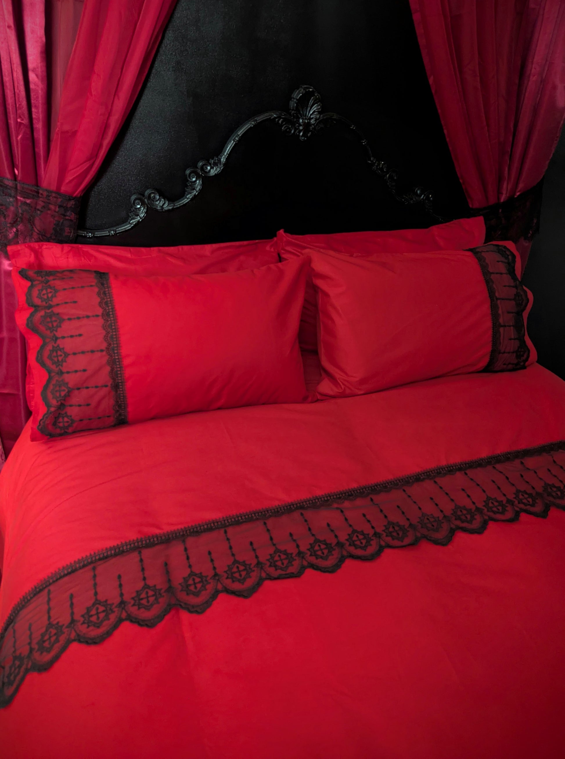 Red bedding set with black lace trim on a bed with red curtains.