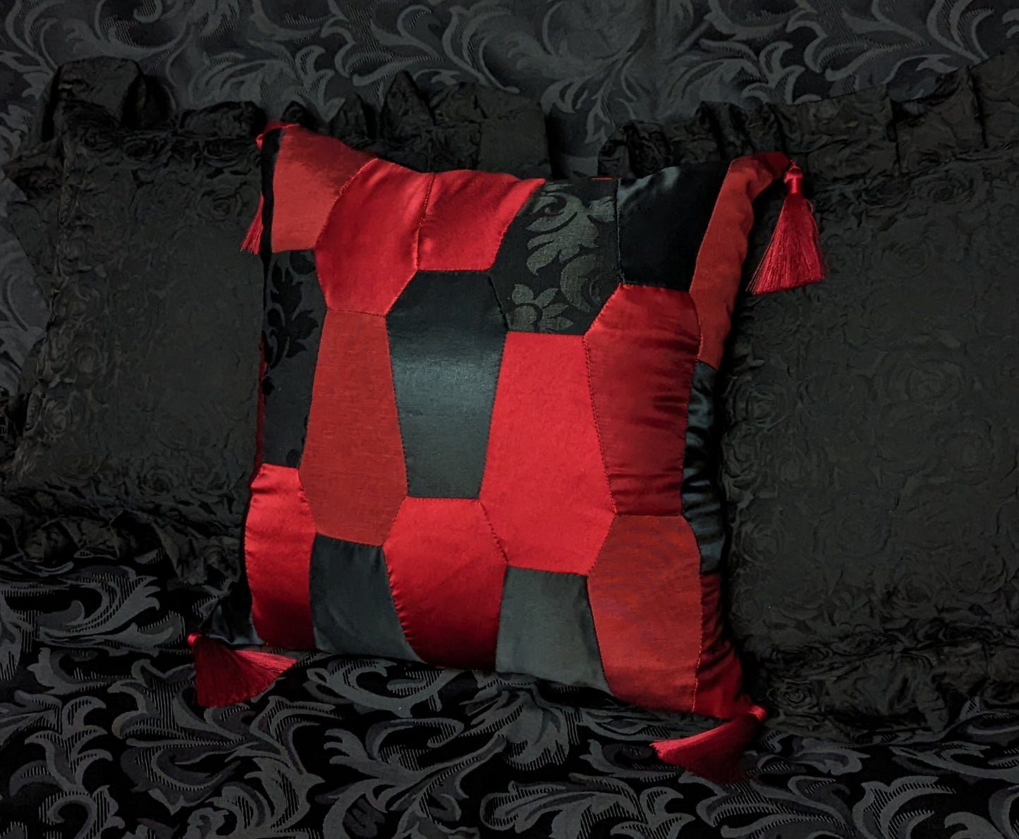 Cushion made of red and black satin fabrics in coffin shapes with red tassels on the corners.