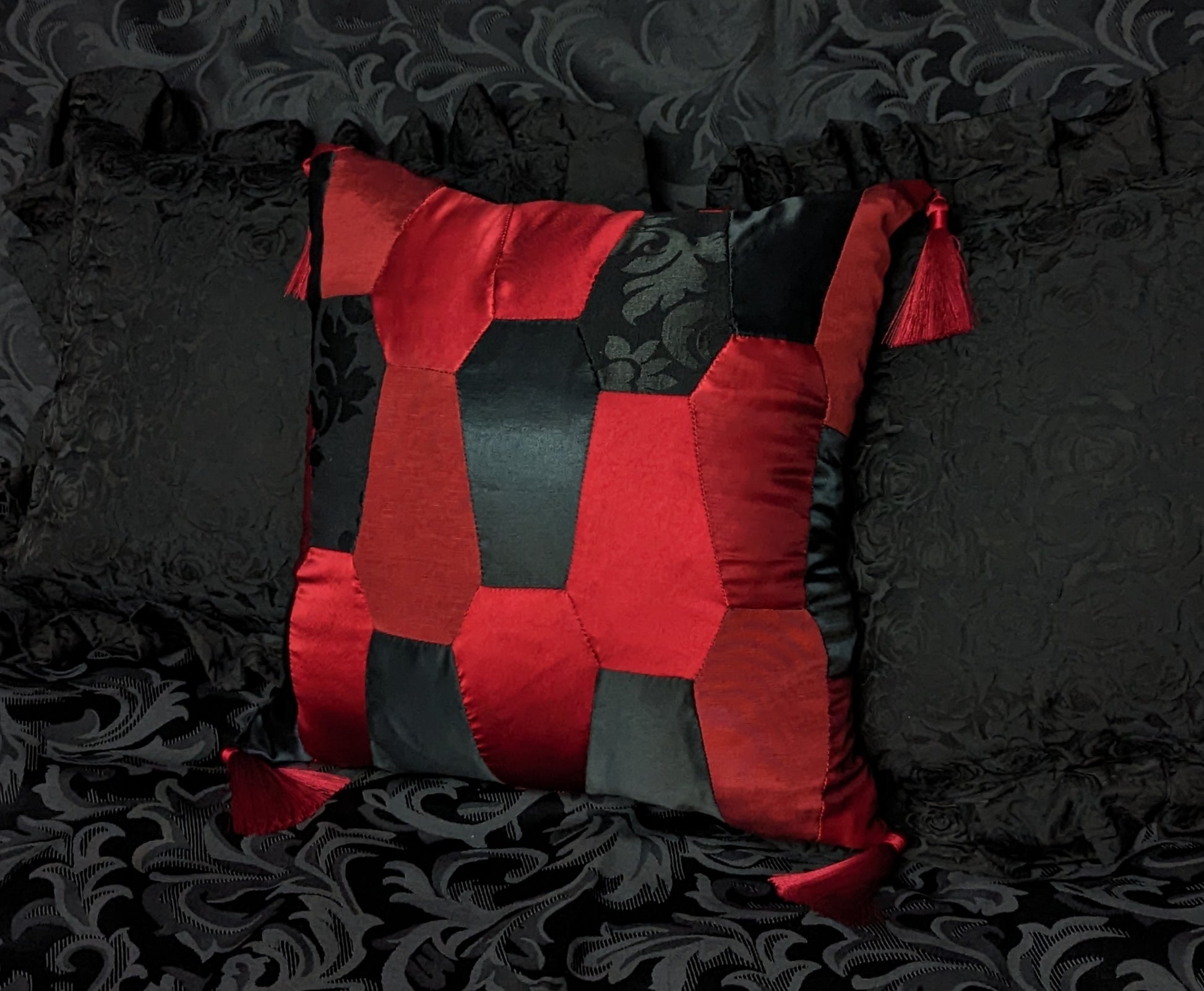 Cushion made of red and black satin fabrics in coffin shapes with red tassels on the corners.